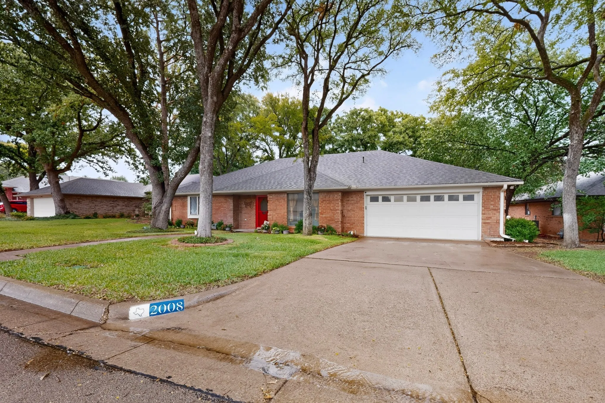 Brick exterior with a white garage door, concrete driveway, and a red front door