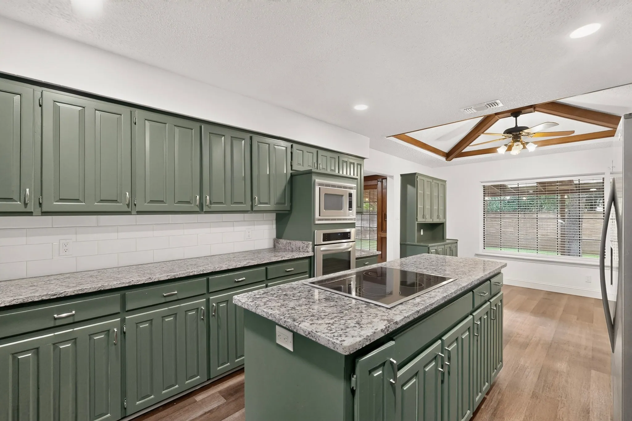 Kitchen featuring extensive cabinetry, stone countertops, a tile backsplash, and a central island with an integrated cooktop