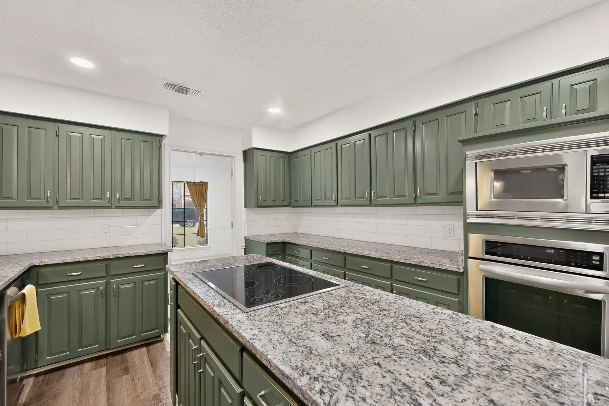 Kitchen featuring extensive green cabinetry, granite countertops, subway tile backsplash, and wood-finish flooring