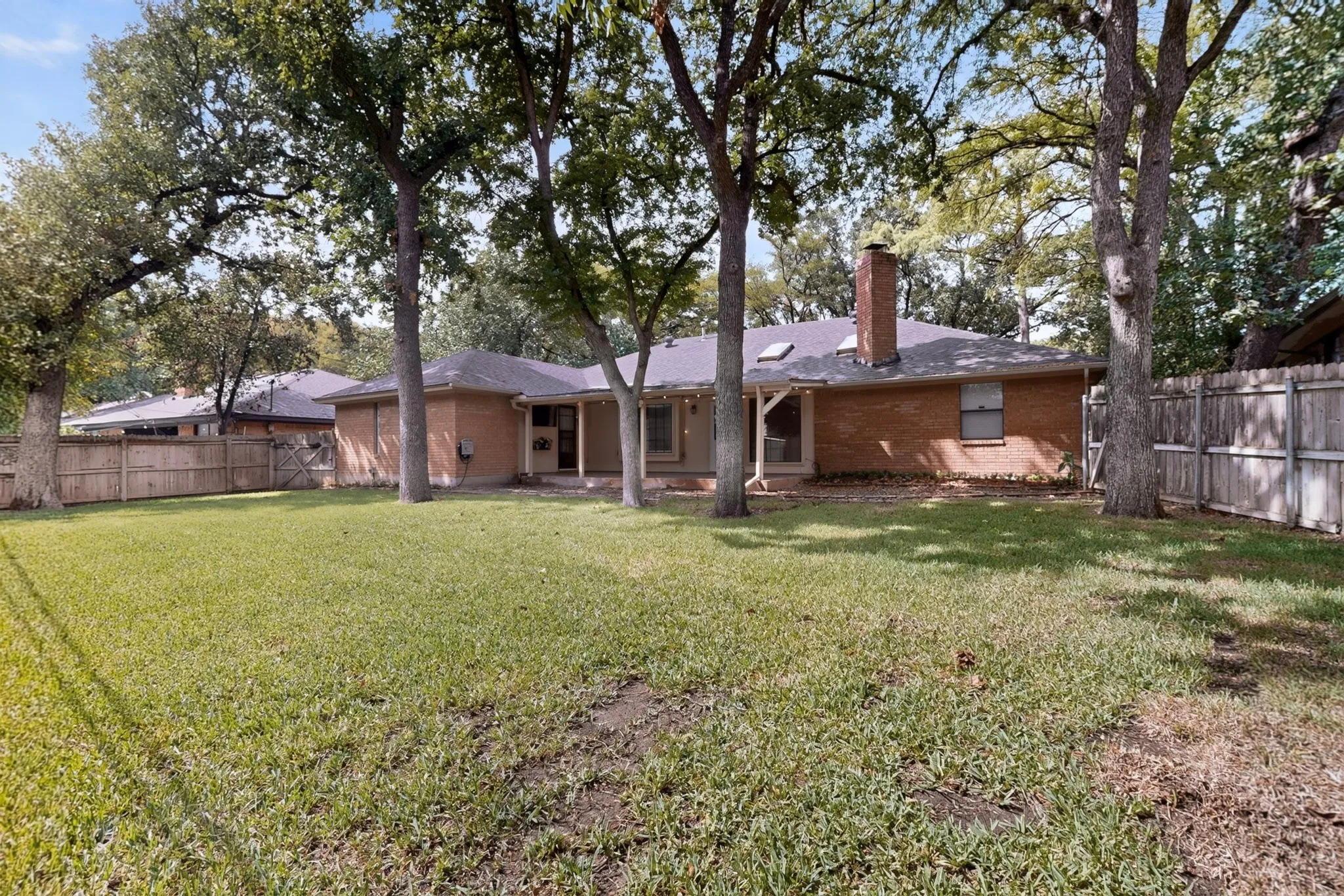 Expansive backyard with mature trees, a wood privacy fence, and multiple access points to the residence