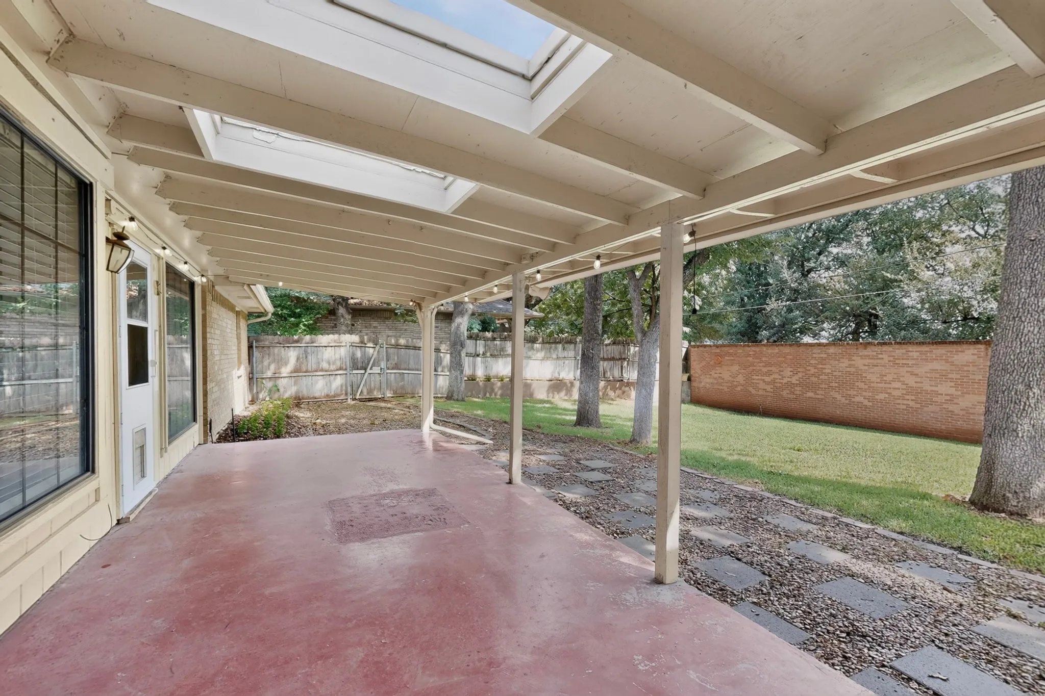 Covered patio with integrated skylights, concrete flooring, and a gravel path