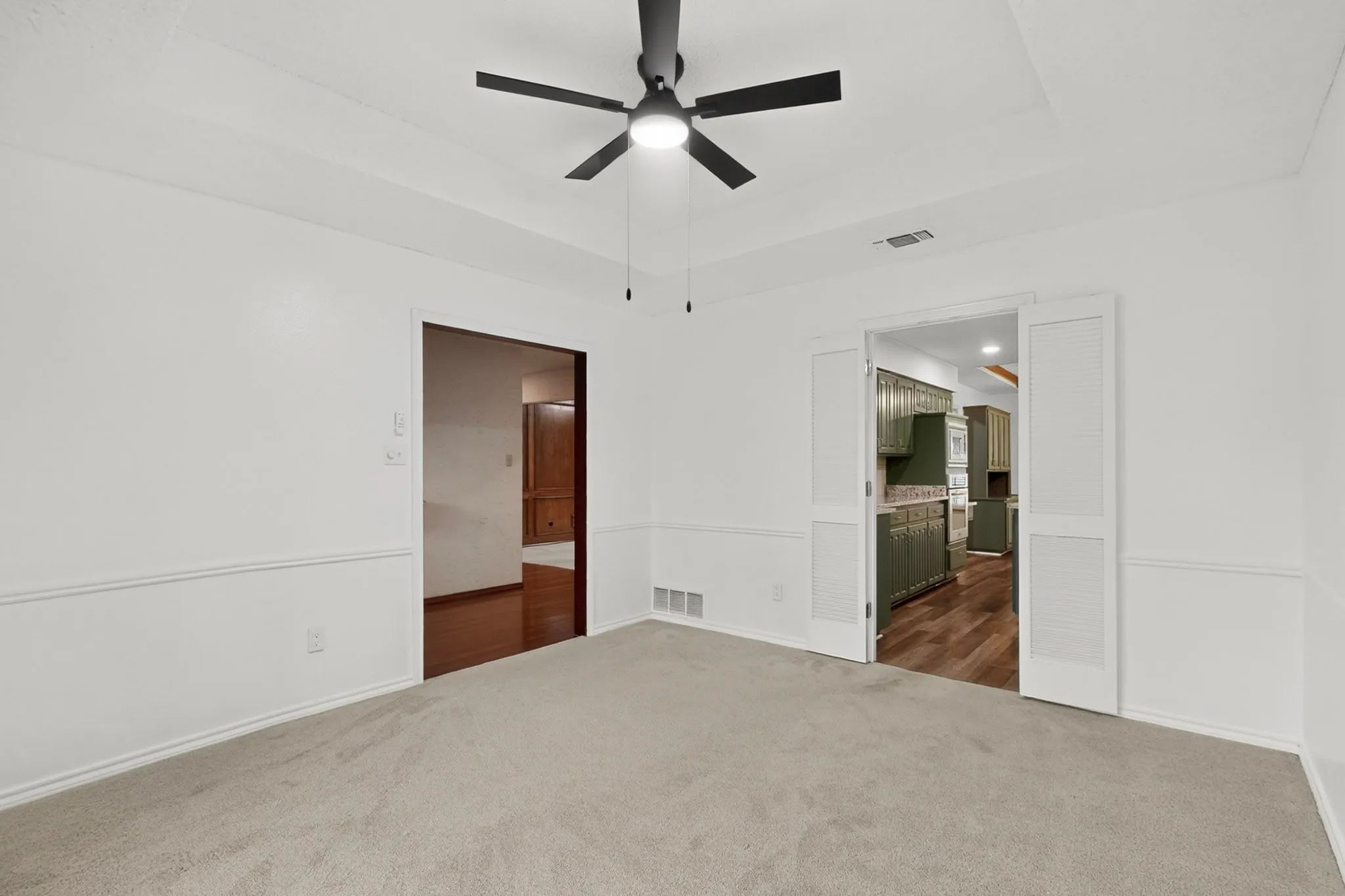 Tray ceiling with recessed lighting and a ceiling fan, white paneled walls, and soft carpeting