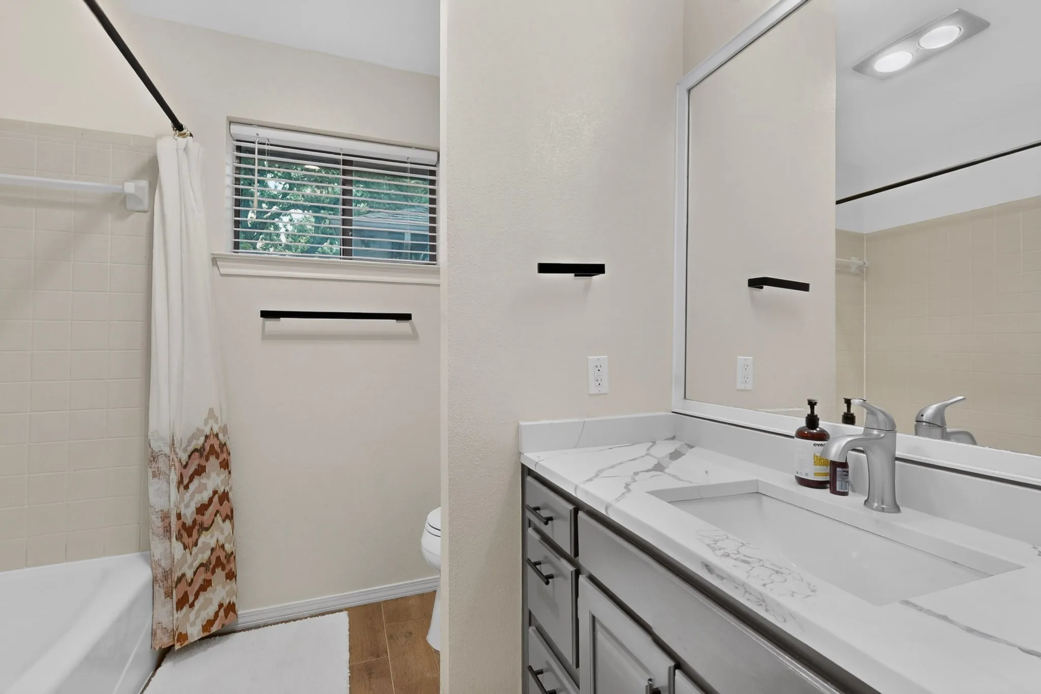 Bathroom featuring a built-in vanity with an integrated sink, a large wall-mounted mirror, a white bathtub, and wood-finish flooring