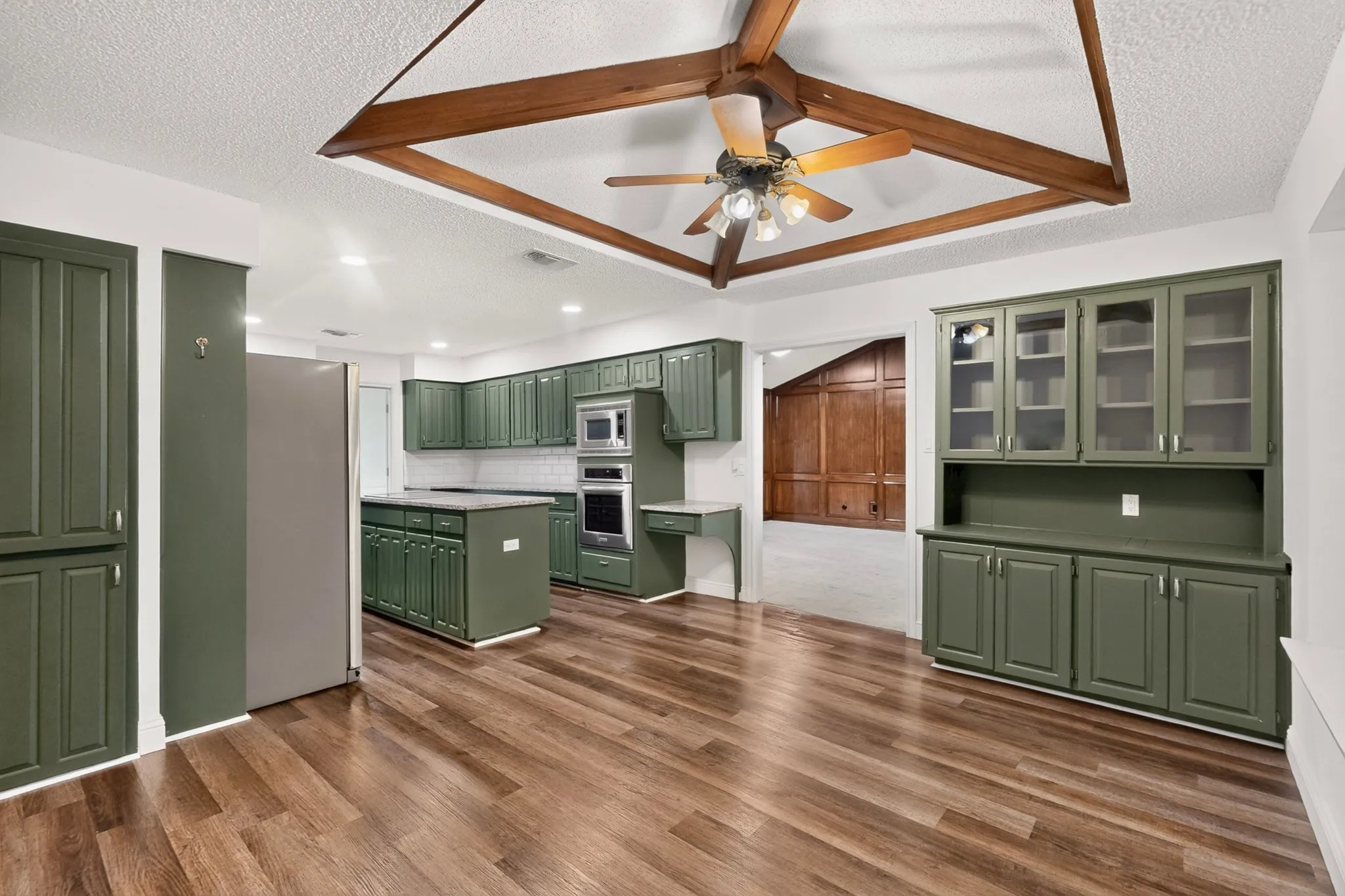Wood-finish flooring throughout, featuring a kitchen island, built-in appliances, and extensive cabinetry with glass-front uppers