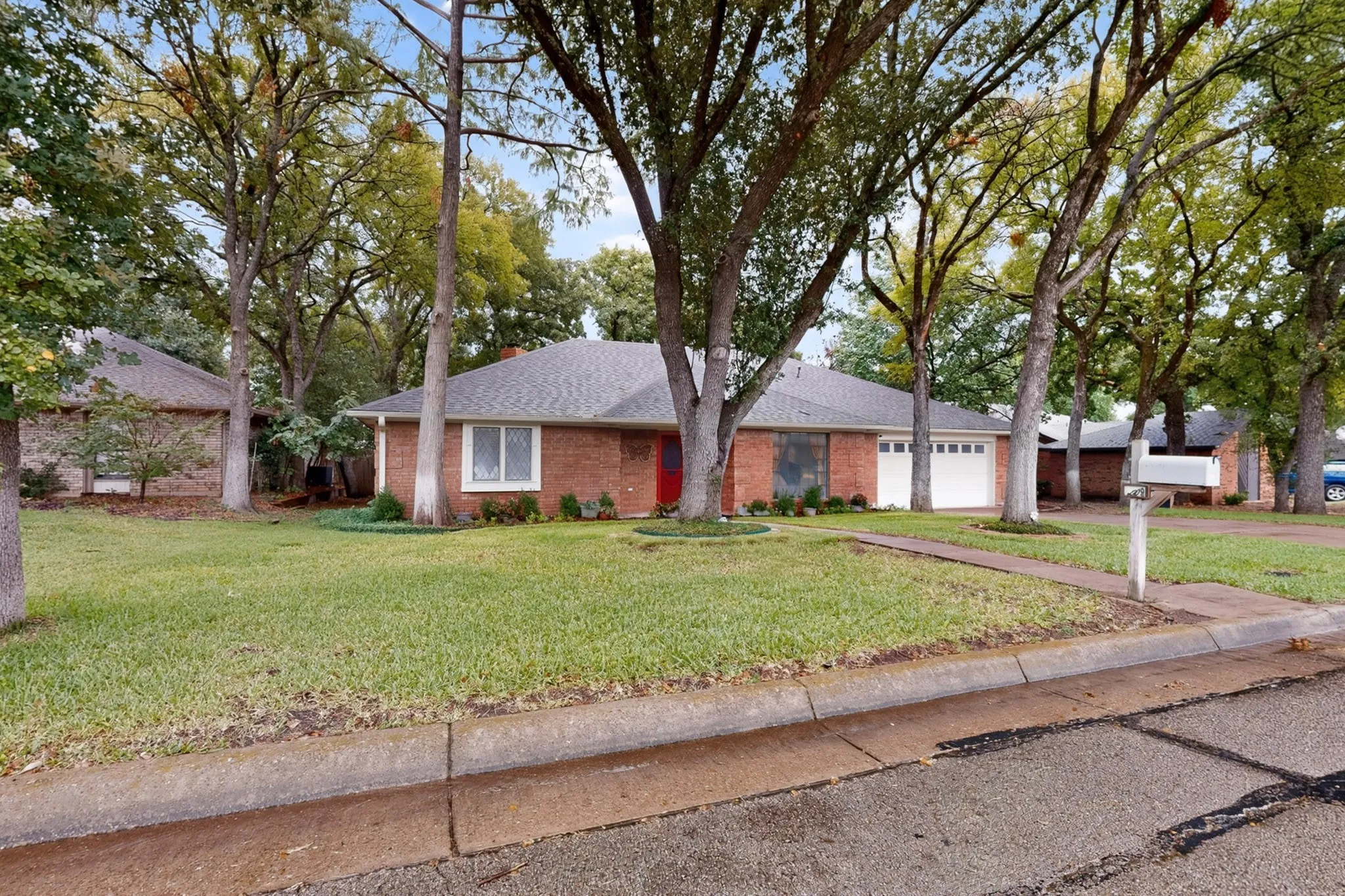 Brick exterior, white-framed windows, attached two-car garage, mature trees, and a manicured lawn