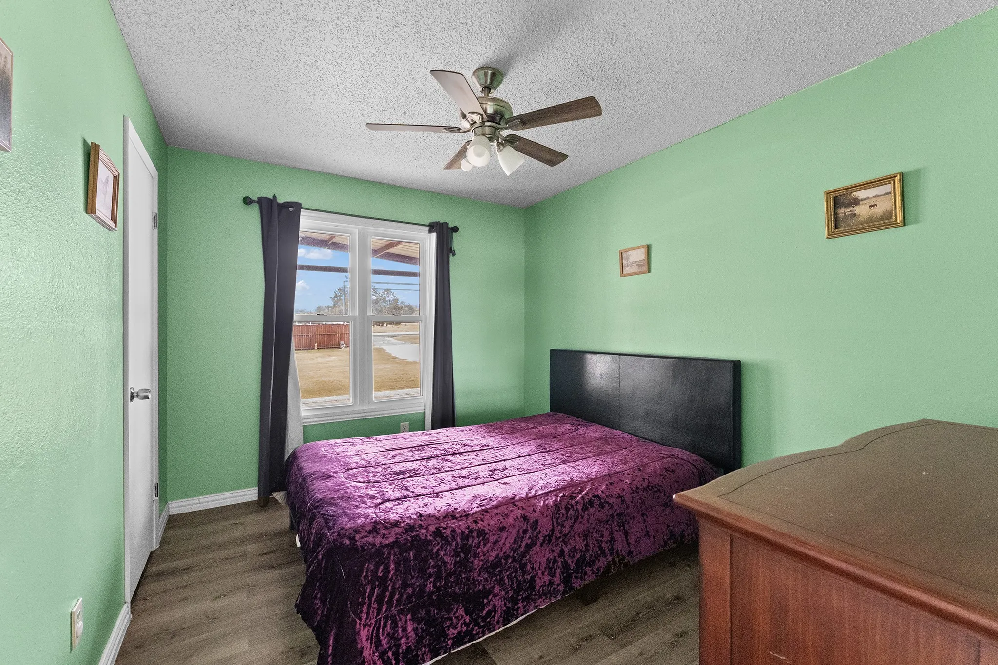 Wood-finish flooring, ceiling fan with integrated lighting, and a window with dark draperies