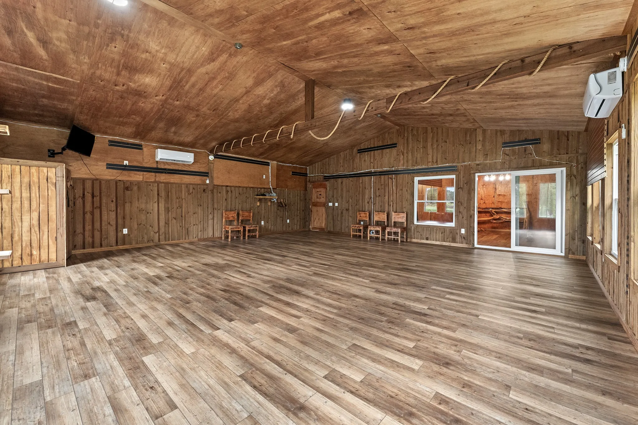 Vaulted wood-paneled ceiling, wood-finish flooring, wood-paneled walls, sliding glass door, multiple fixed windows