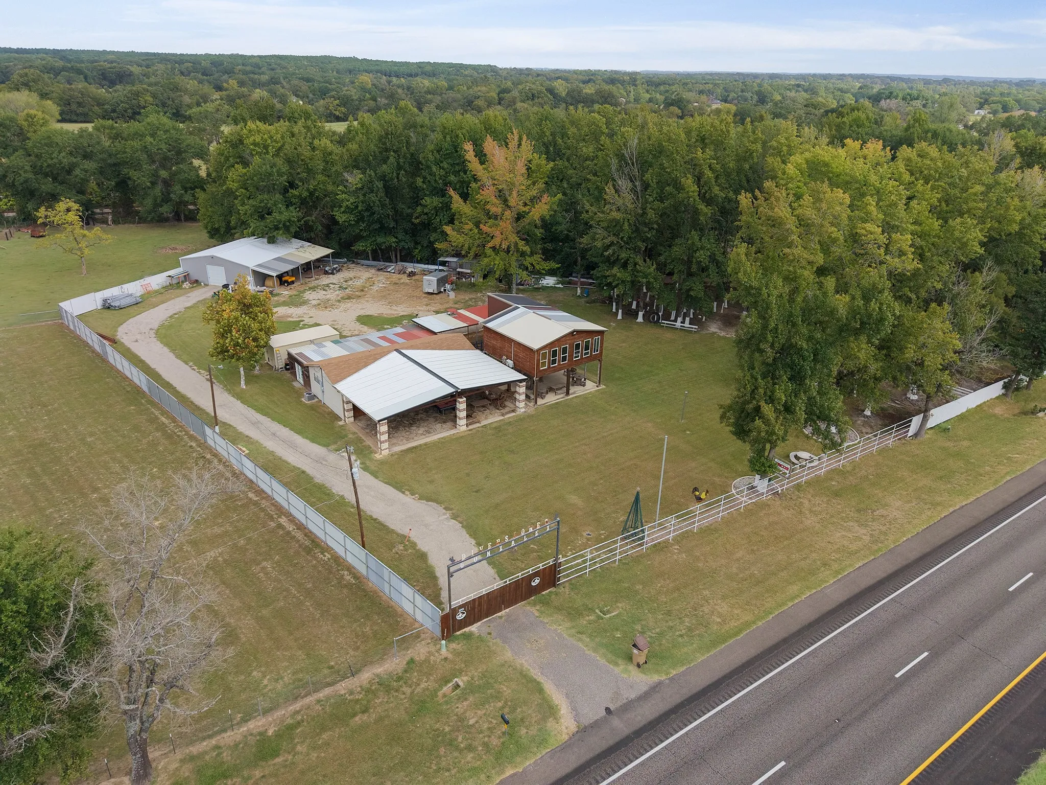 Expansive property featuring a gravel driveway, multiple outbuildings, fenced perimeter, and a wooded backdrop