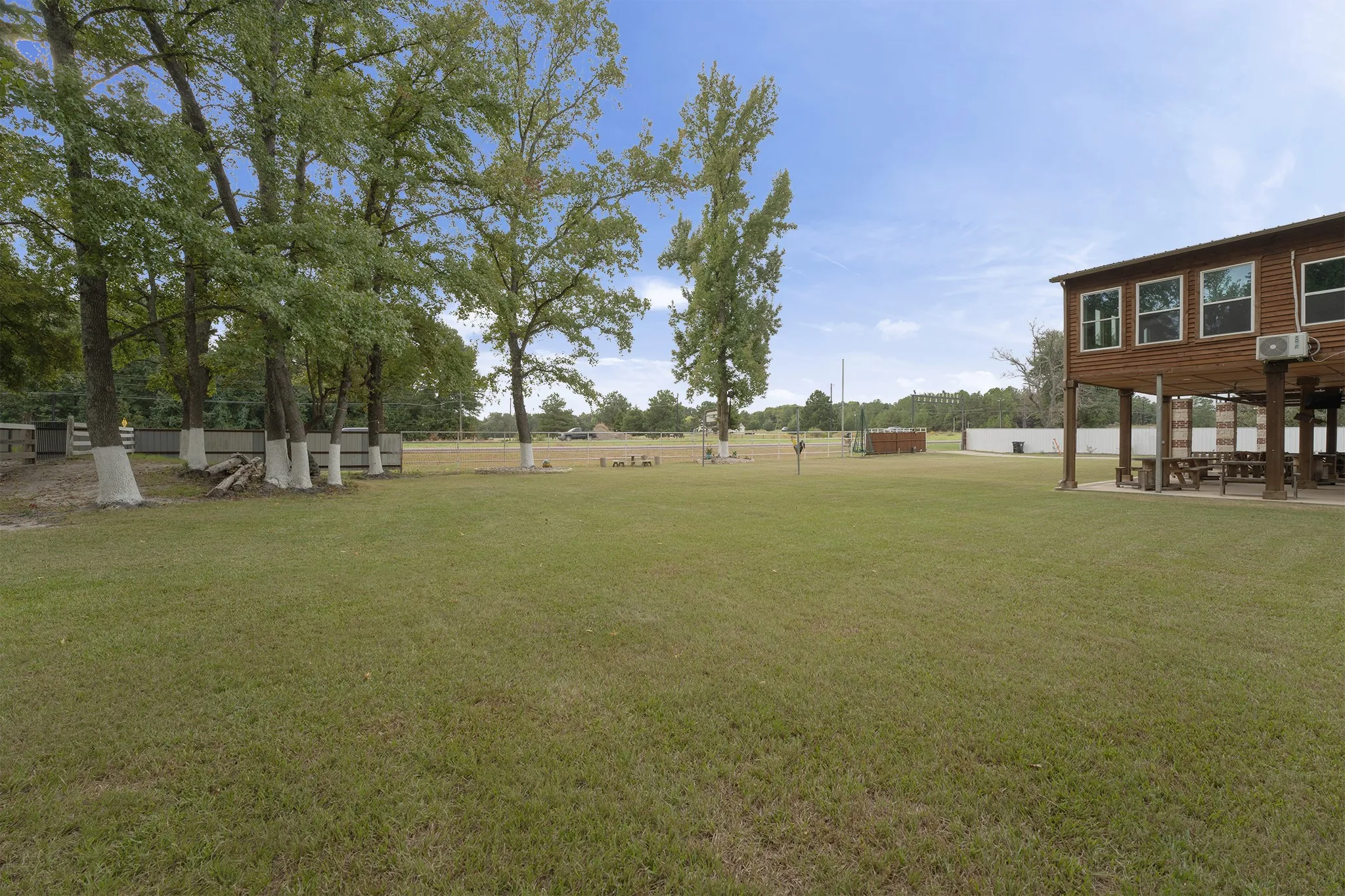 Expansive grassy area with mature trees, a multi-story wood-sided structure, and a fenced perimeter