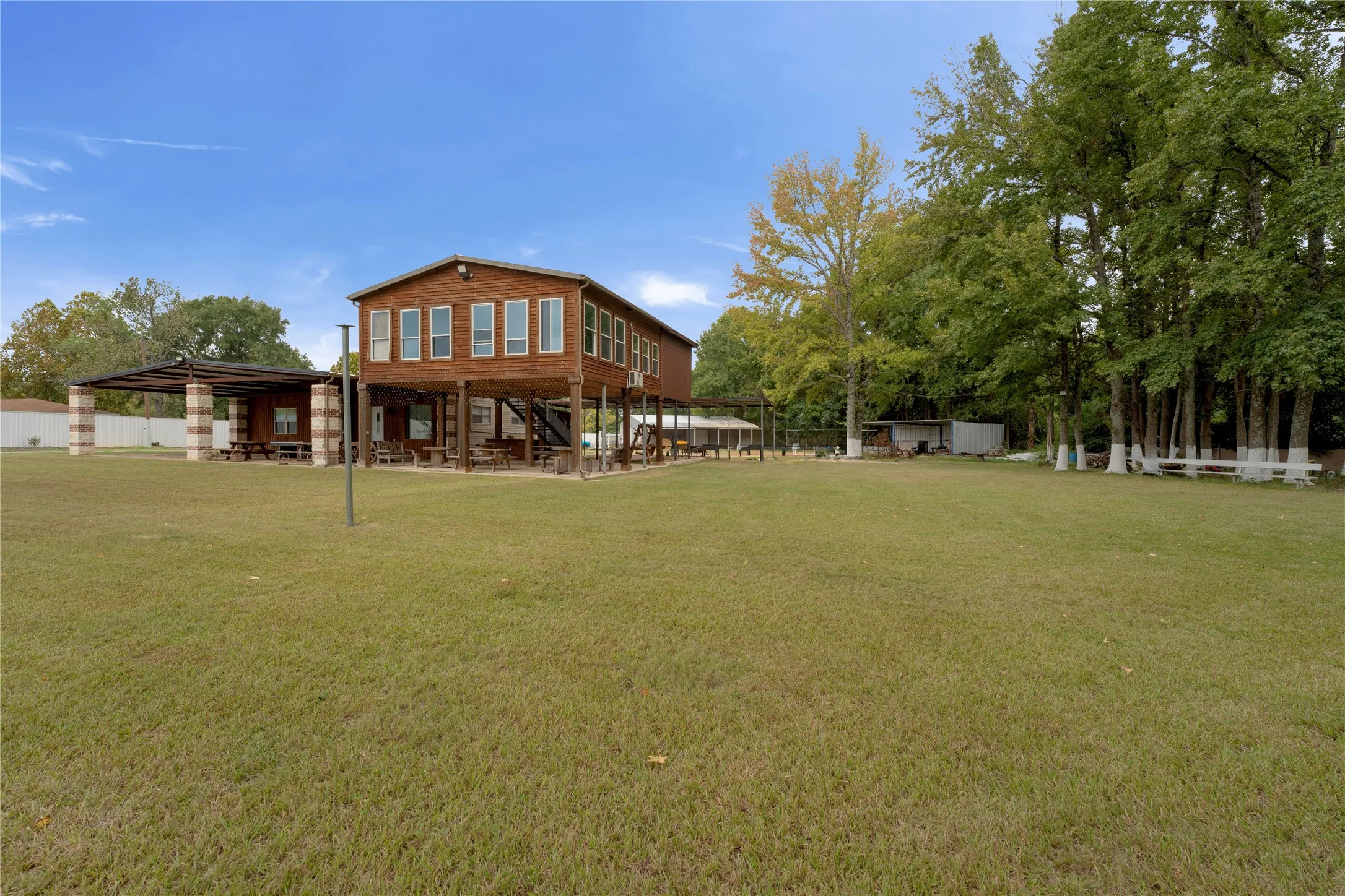 Elevated wooden structure featuring multiple windows, a covered outdoor area with stone-clad columns, and a large grassy expanse