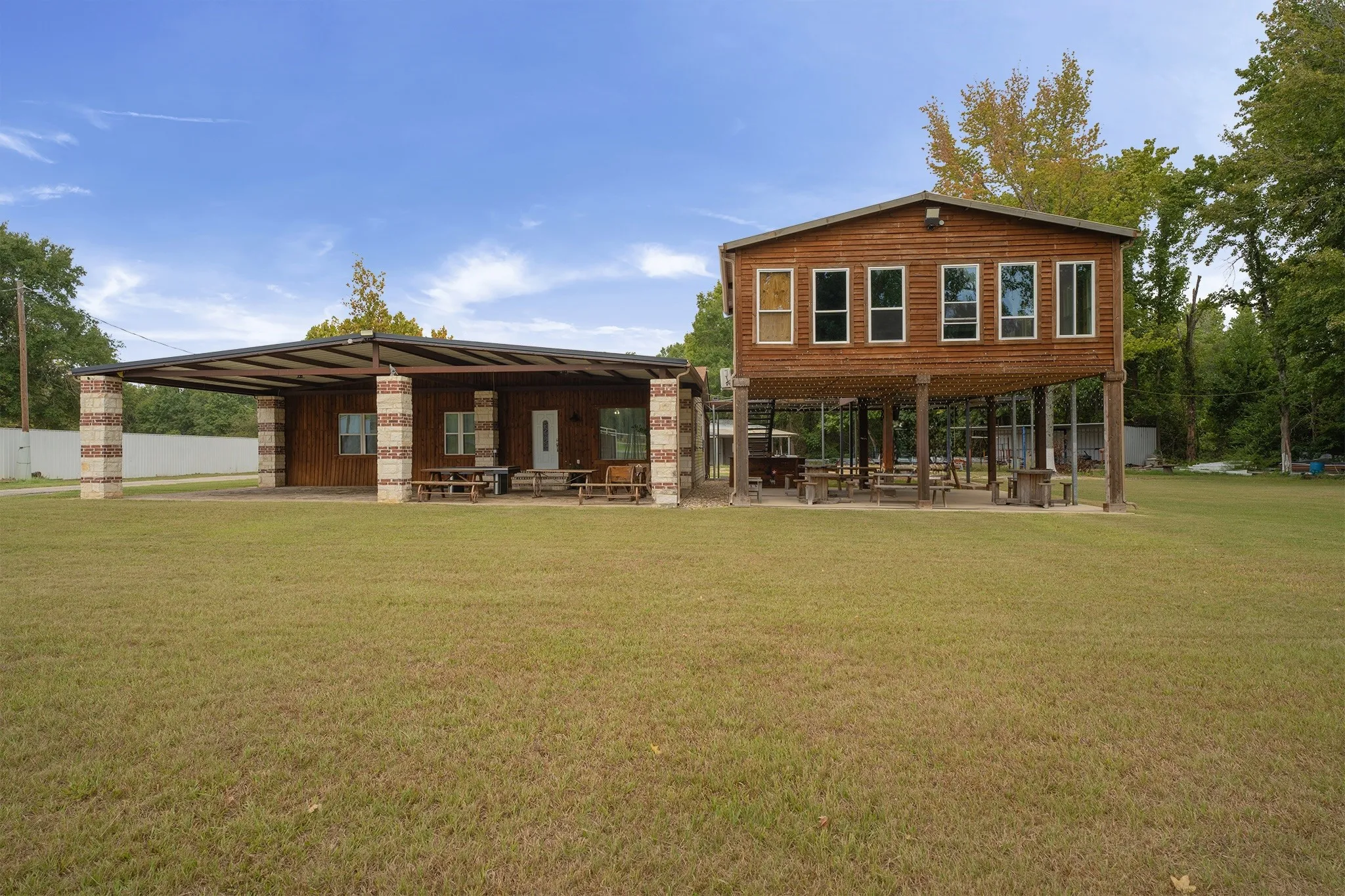 Two-story wood-sided structure featuring an elevated second level, a covered patio with brick and stone pillars, and a metal roof