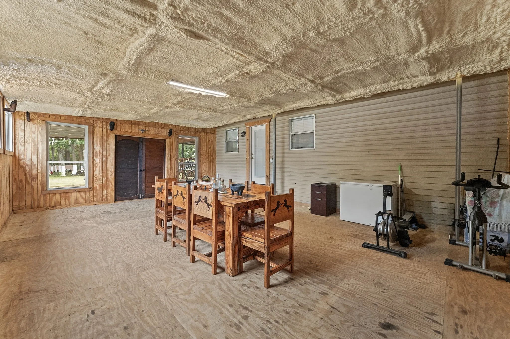Expansive room with plywood flooring, wood-paneled walls, and a textured ceiling
