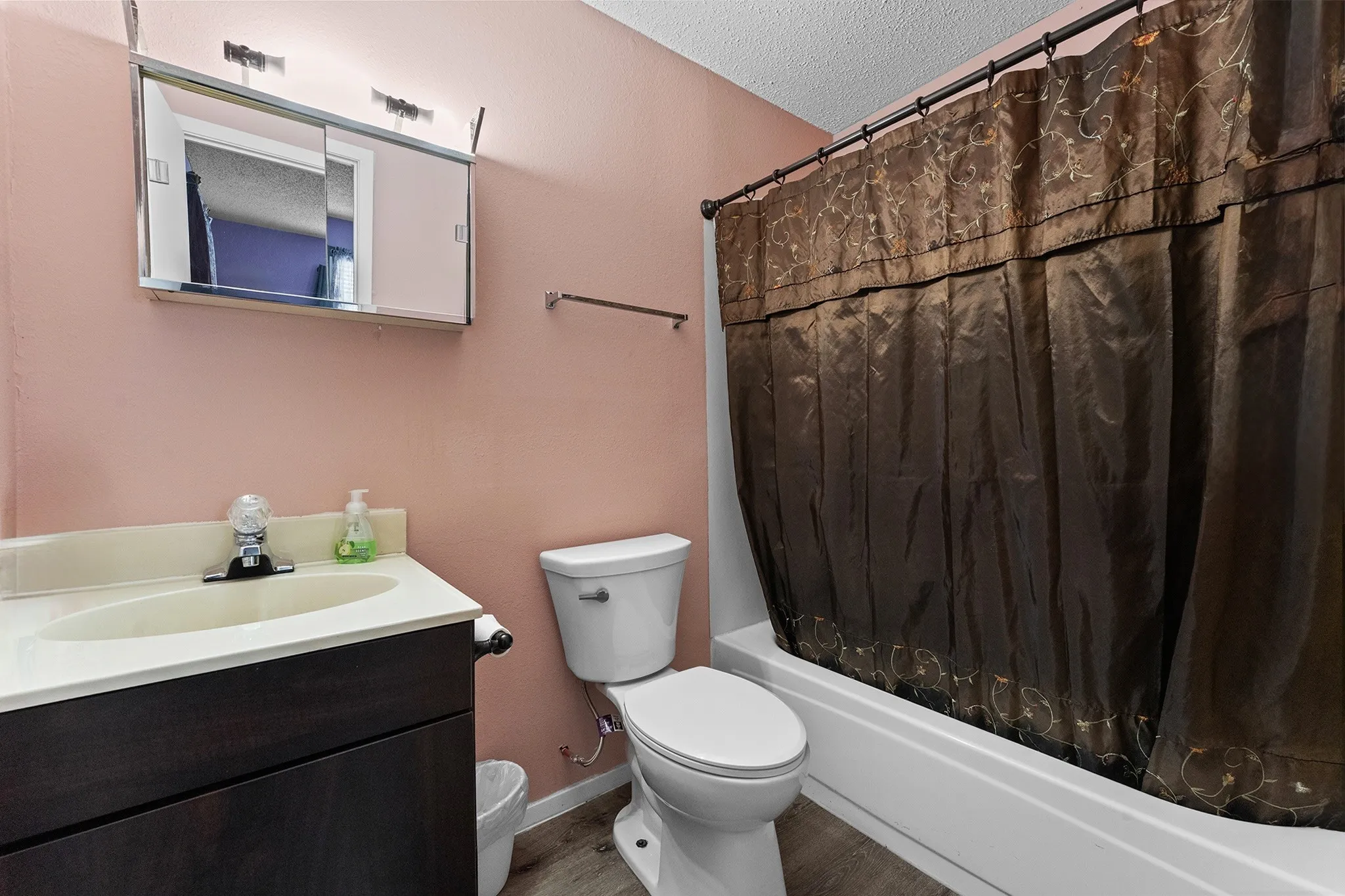 Vanity with integrated sink, coordinating wall-mounted mirror with lighting, and a white bathtub with a shower curtain rod