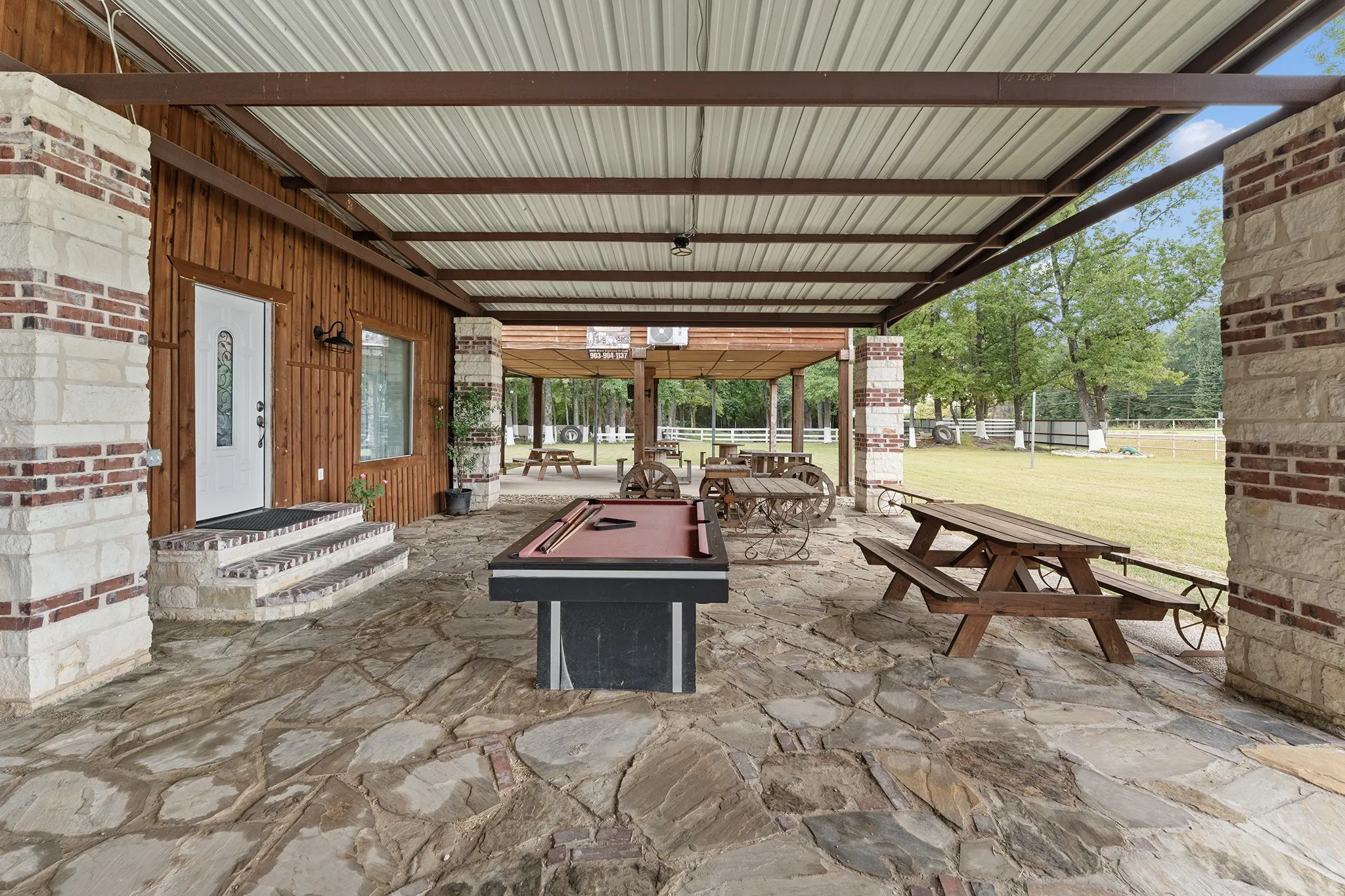 Expansive covered patio featuring a metal roof, flagstone flooring, and stone columns with brick accents