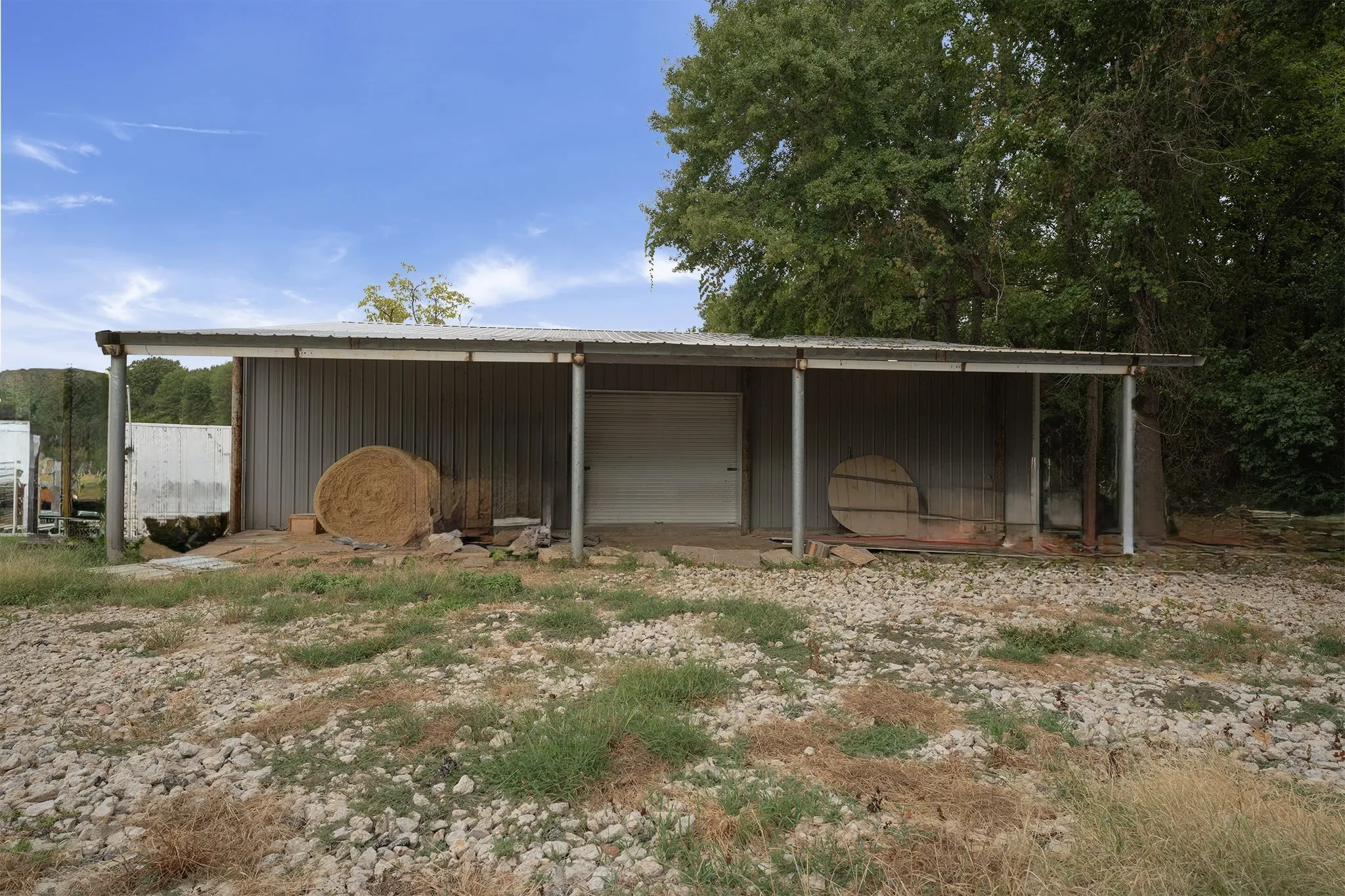 Detached metal structure with a covered extension, featuring a roll-up door and a metal roof