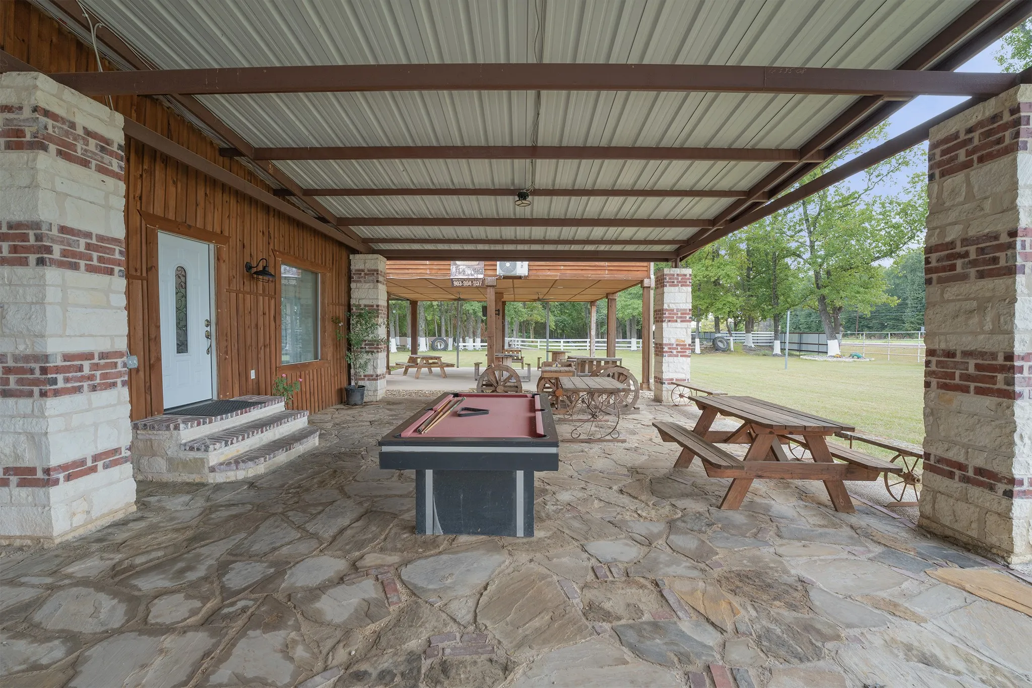 Expansive covered patio featuring flagstone flooring, wood paneling, and stone columns with brick accents