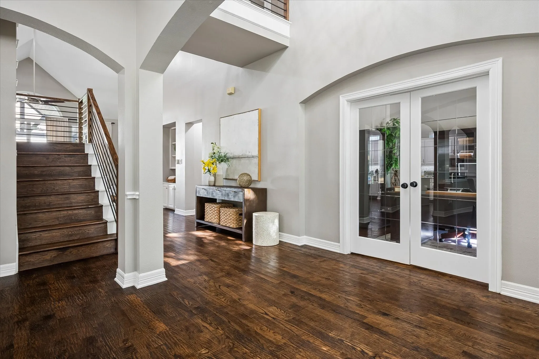Hardwood flooring, arched doorways, a staircase with metal and wood-finish railings, and white-framed glass French doors