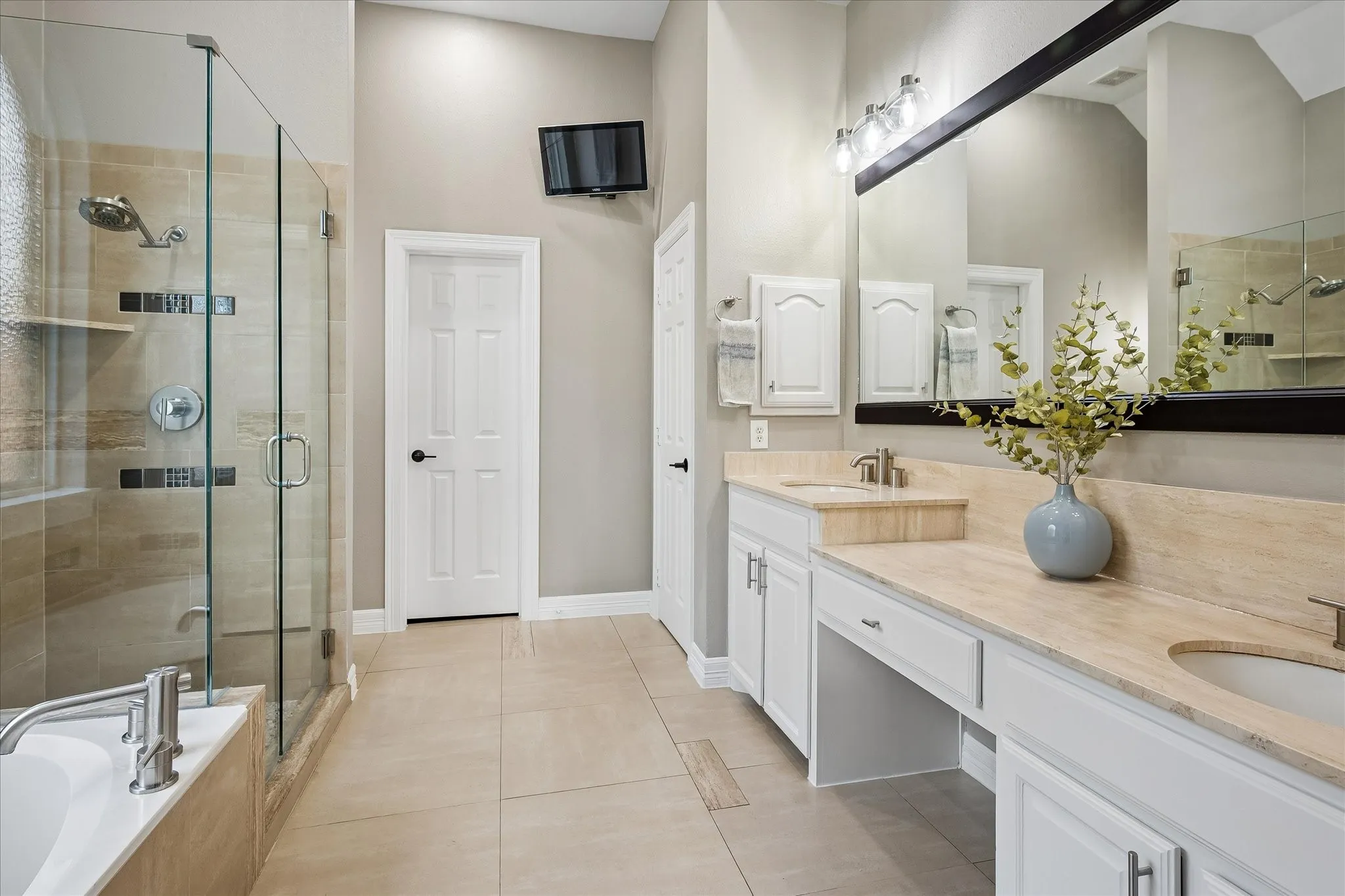 Spacious bathroom featuring a double vanity with stone countertops, white cabinetry, a large frameless glass shower enclosure, and a built-in bathtub