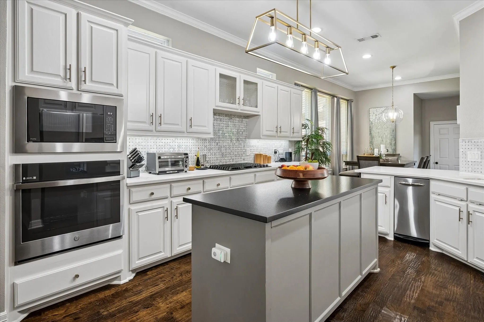 White cabinetry with brushed nickel hardware, stainless steel appliances, dark wood-finish flooring, a kitchen island with a dark countertop, and a tiled backsplash