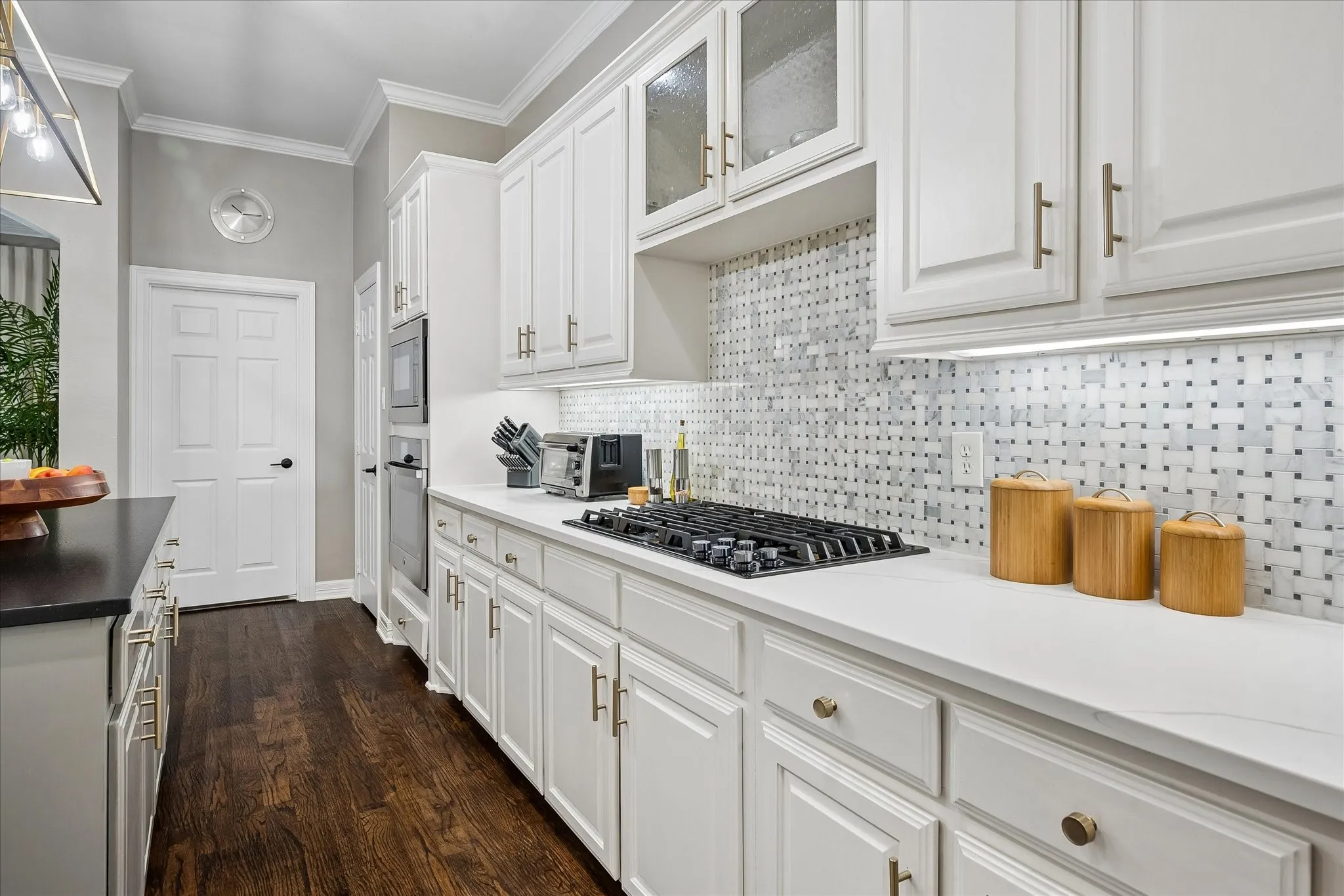 White cabinetry with gold-tone hardware, gas cooktop, patterned tile backsplash, dark wood-finish flooring, and white countertops