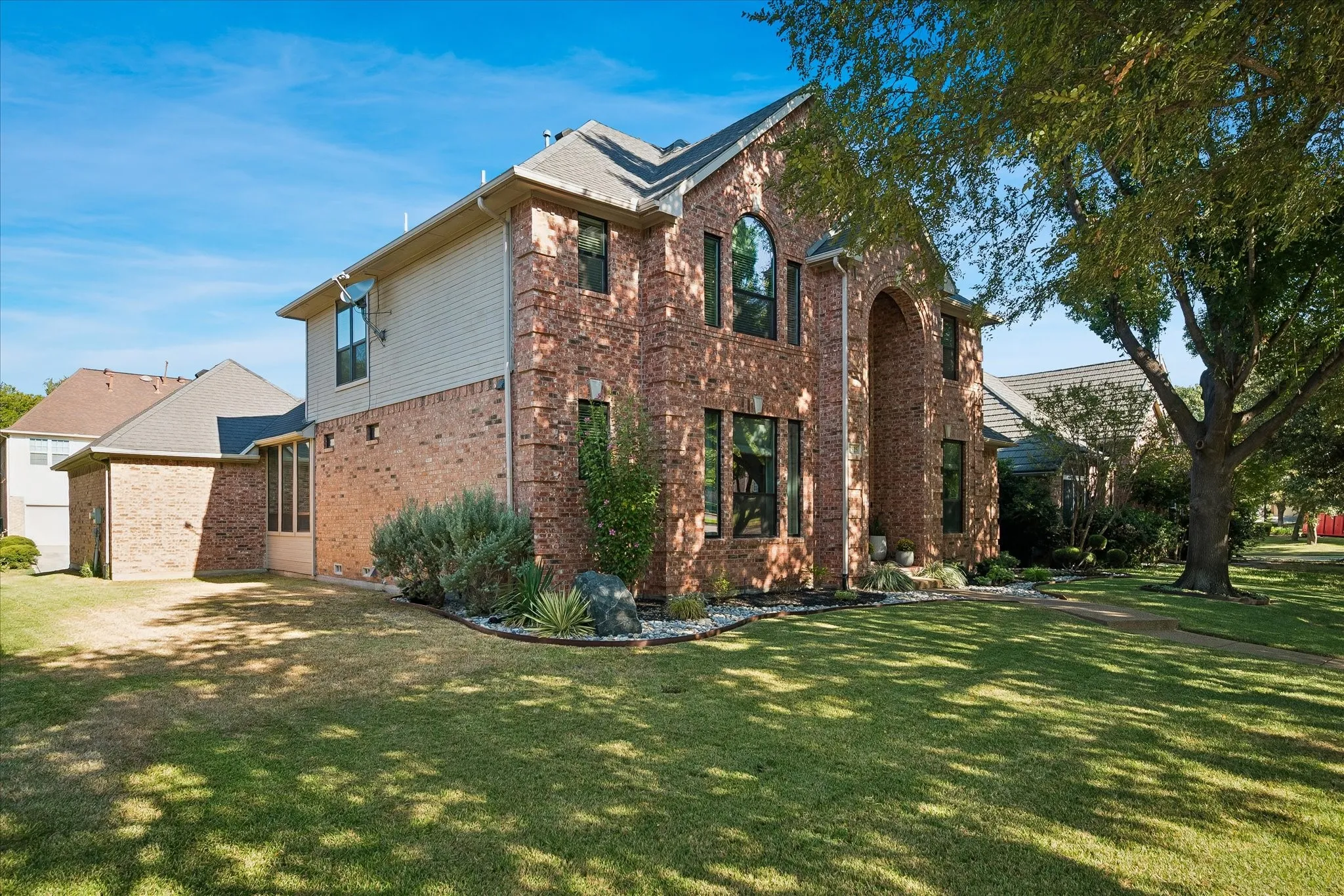 Brick exterior with an arched entryway, multiple windows, and a manicured lawn