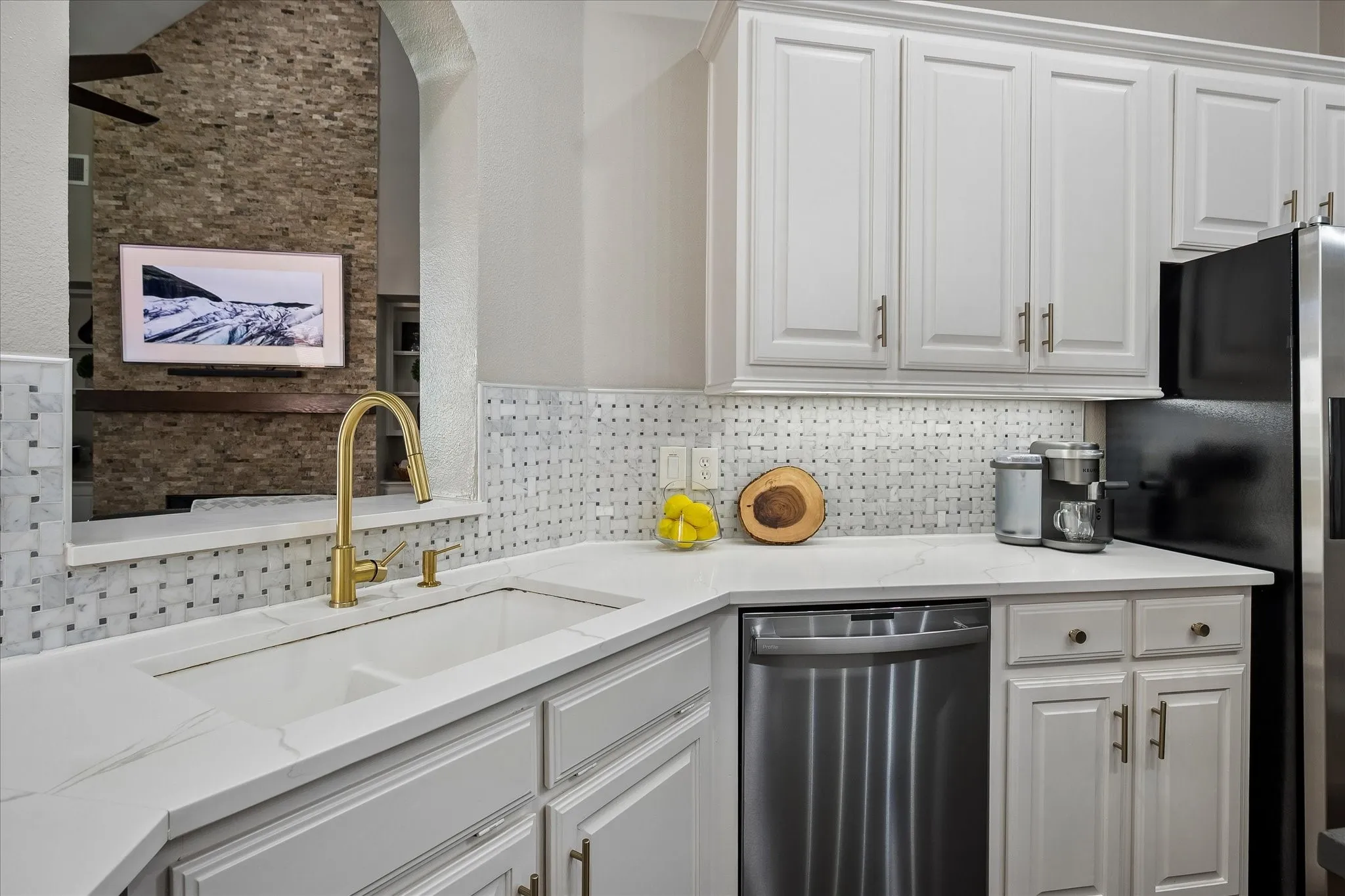White cabinetry with gold-tone hardware, white countertop surfaces, and a mosaic tile backsplash