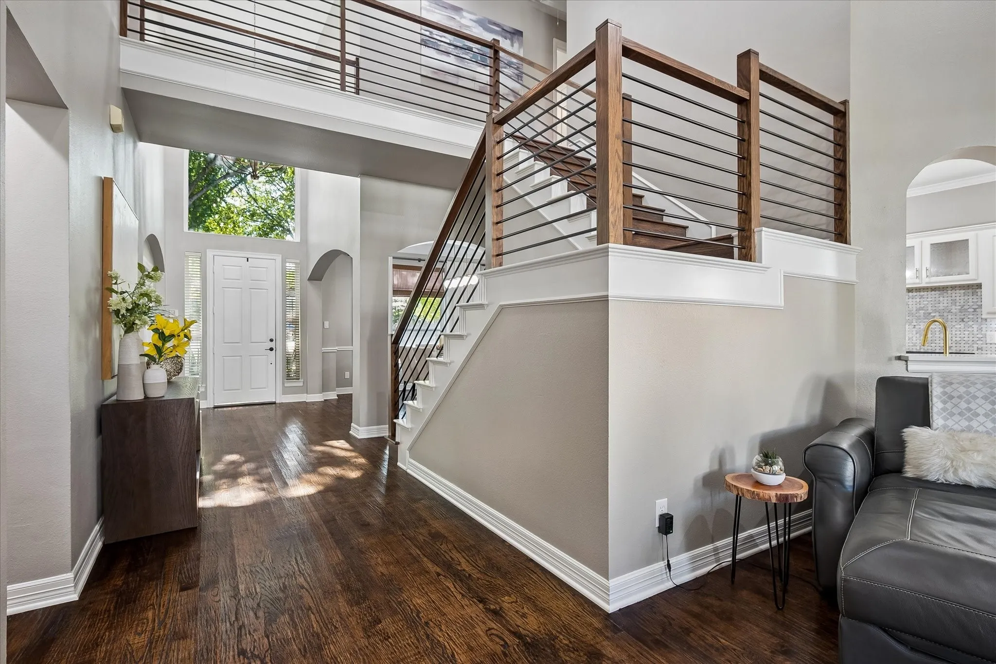 Two-story entryway with wood-finish flooring, a modern wood and metal staircase, arched doorways, and a transom window above the entry door