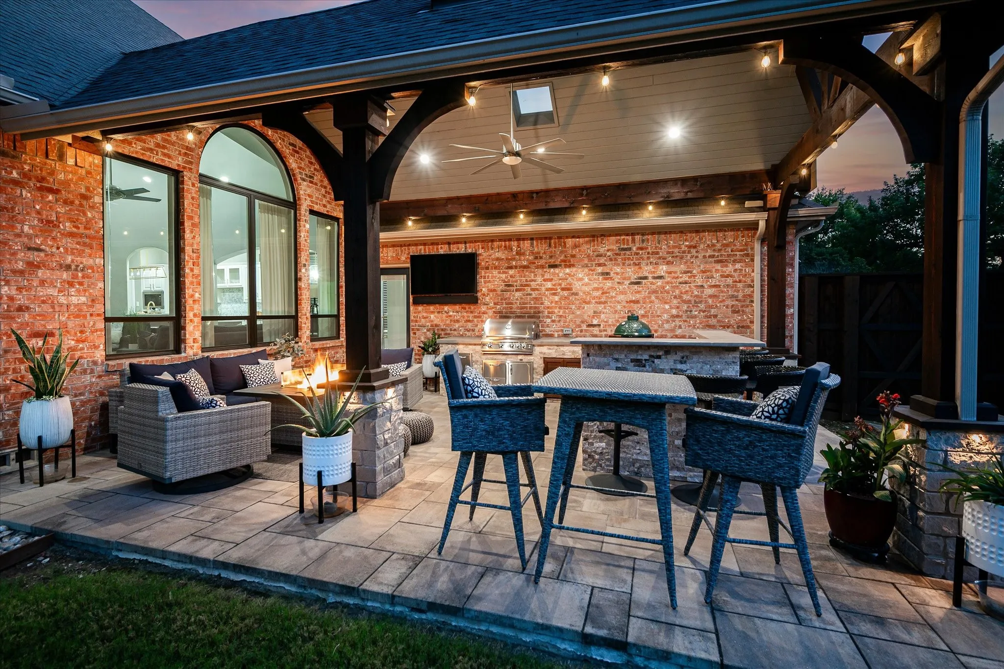Covered outdoor living space featuring brick exterior, paver patio, wood beam ceiling, built-in outdoor kitchen, and arched windows