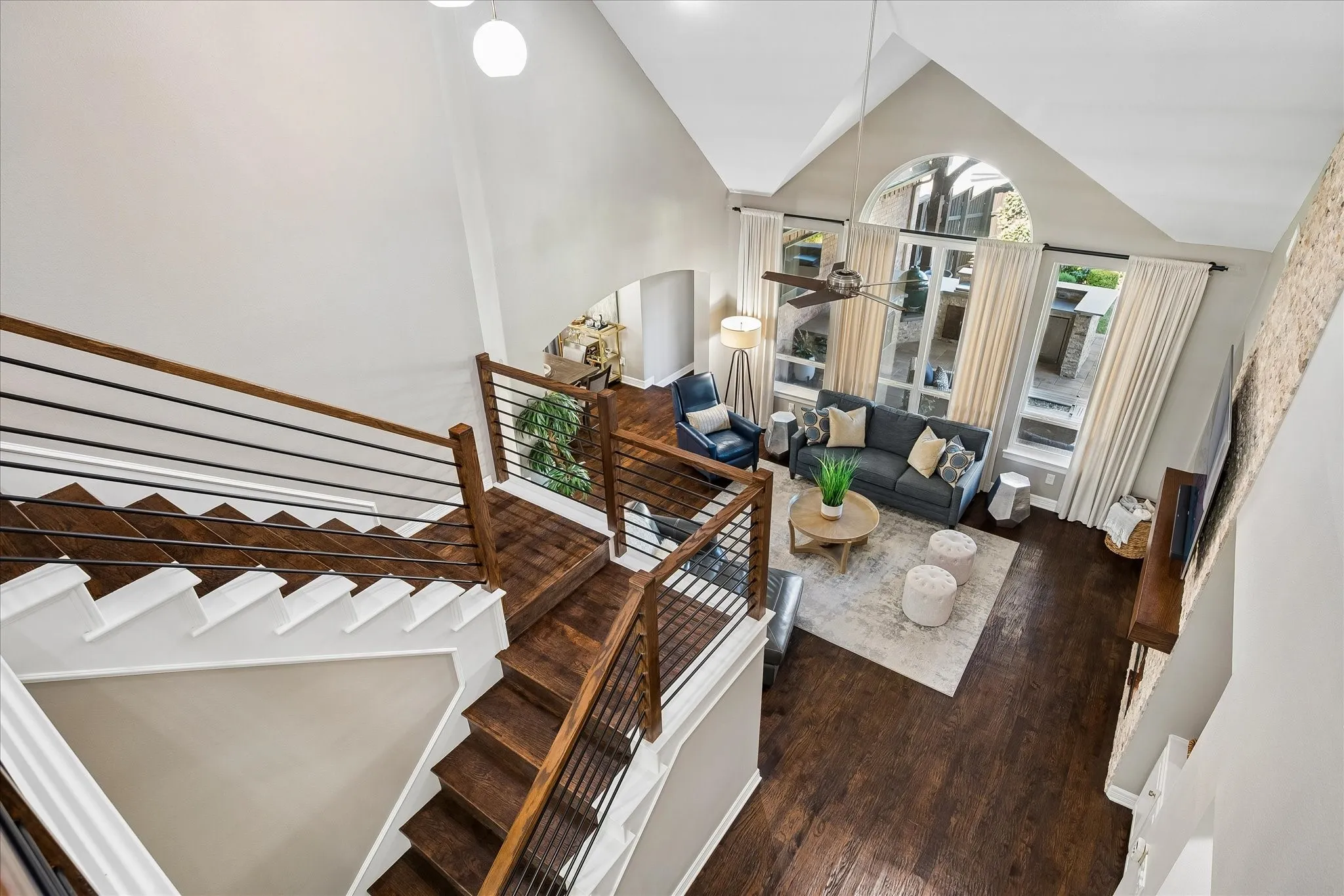Vaulted ceilings with an arched window, wood-finish flooring, staircase with metal spindles, and a ceiling fan