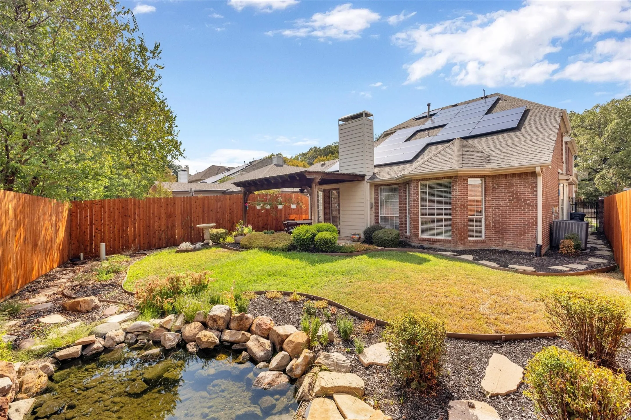 Brick exterior with solar panels, a wood privacy fence, and a pergola-covered patio