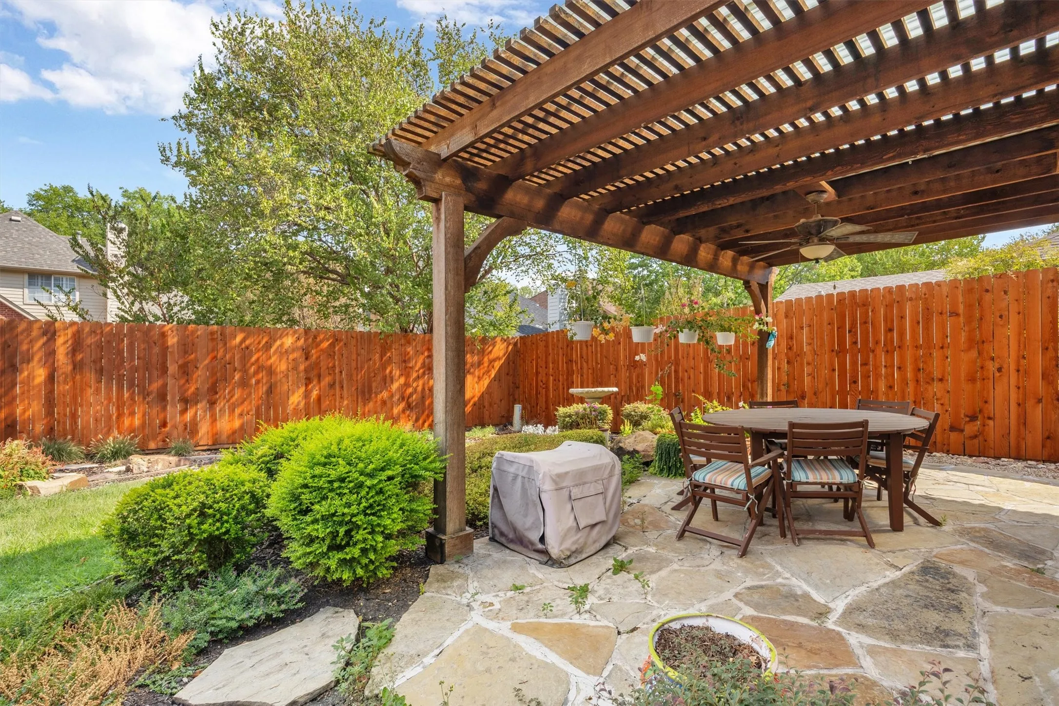 Flagstone patio with a wood pergola, integrated ceiling fan, wood privacy fence, and established landscaping