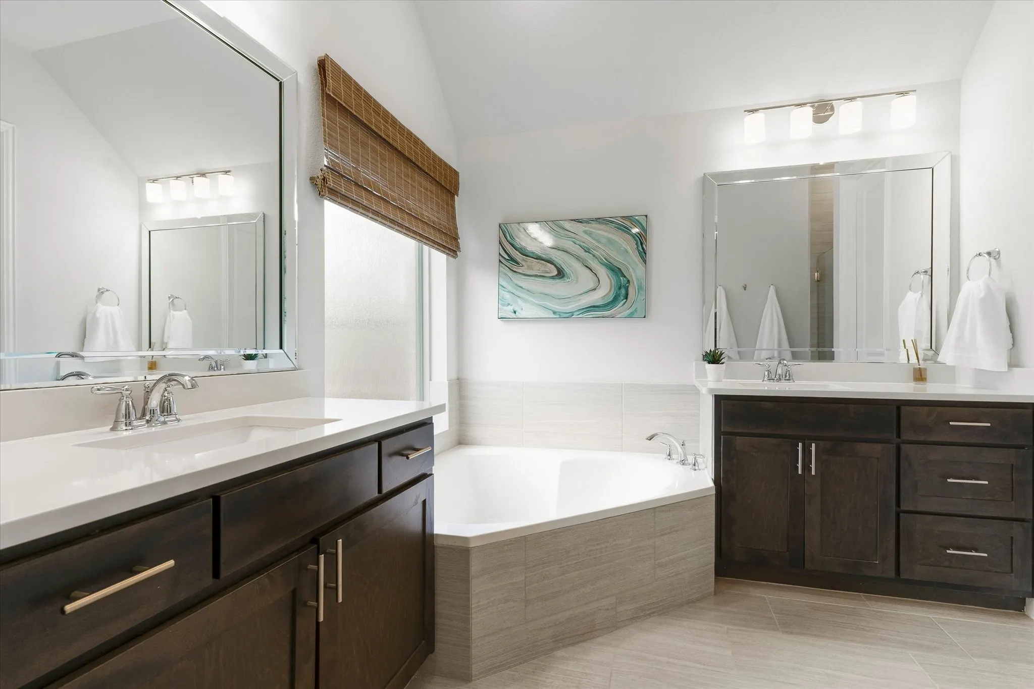 Dual vanities with white countertops, deep soaking tub, wood-finish cabinetry, and tiled flooring