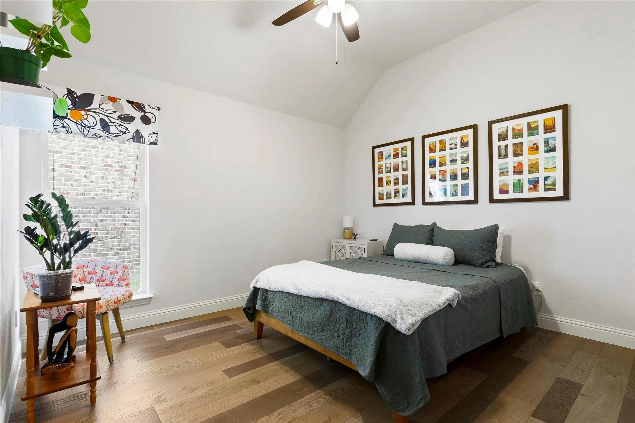 Vaulted ceiling, wood-finish flooring, white walls, large window, and a ceiling fan