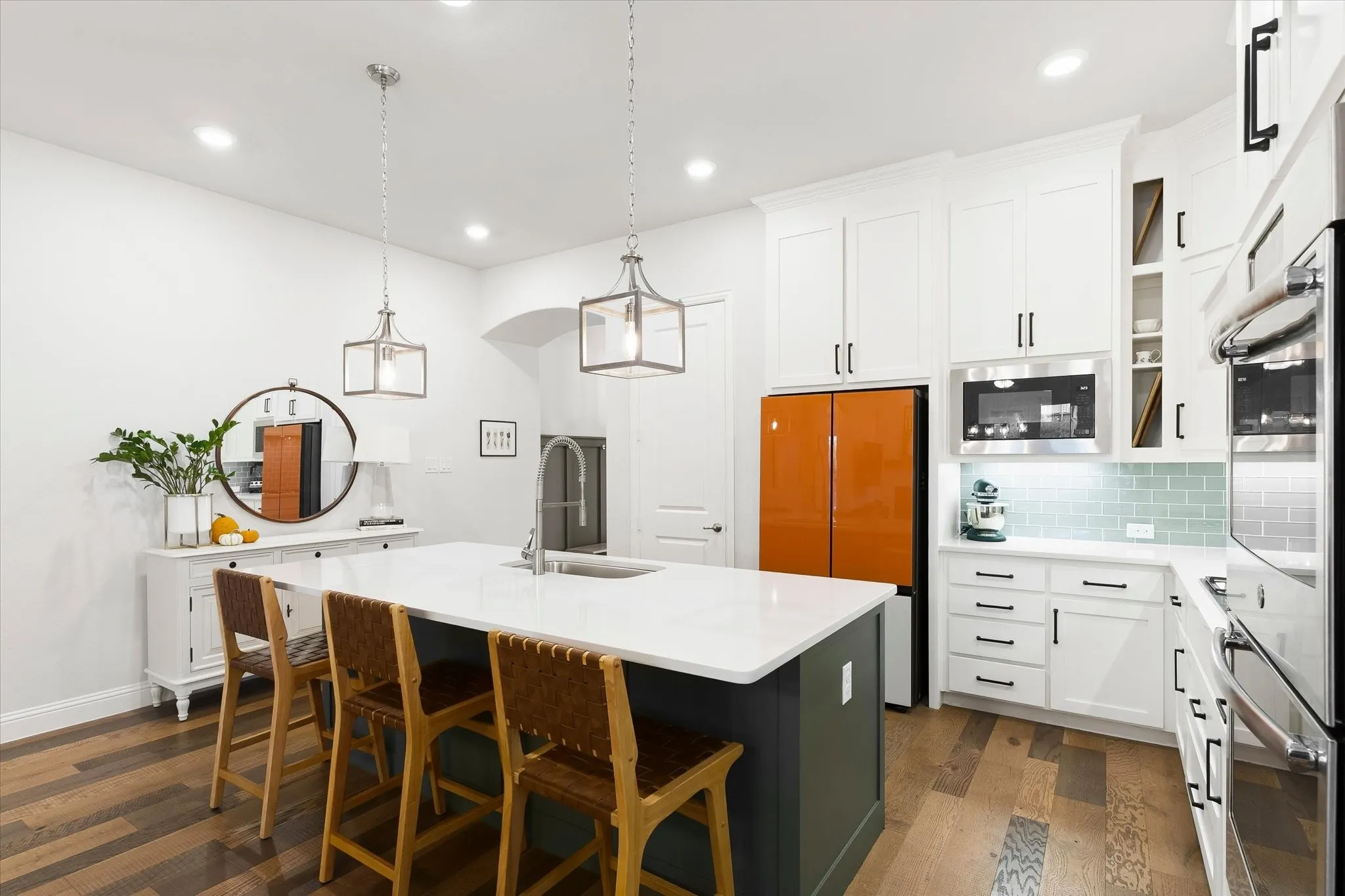 Open-concept kitchen featuring an oversized island with seating, white shaker cabinetry, stainless steel appliances, and wood-finish flooring