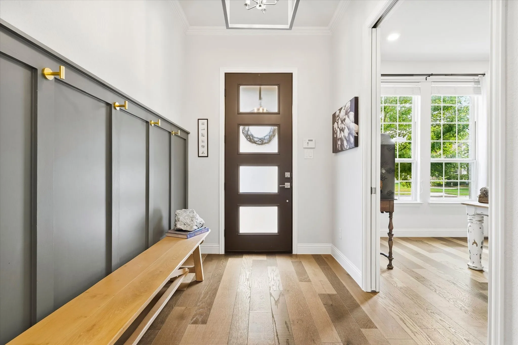 Entryway featuring wood-finish flooring, a contemporary front door with frosted glass panels, and a built-in wall paneling with hooks