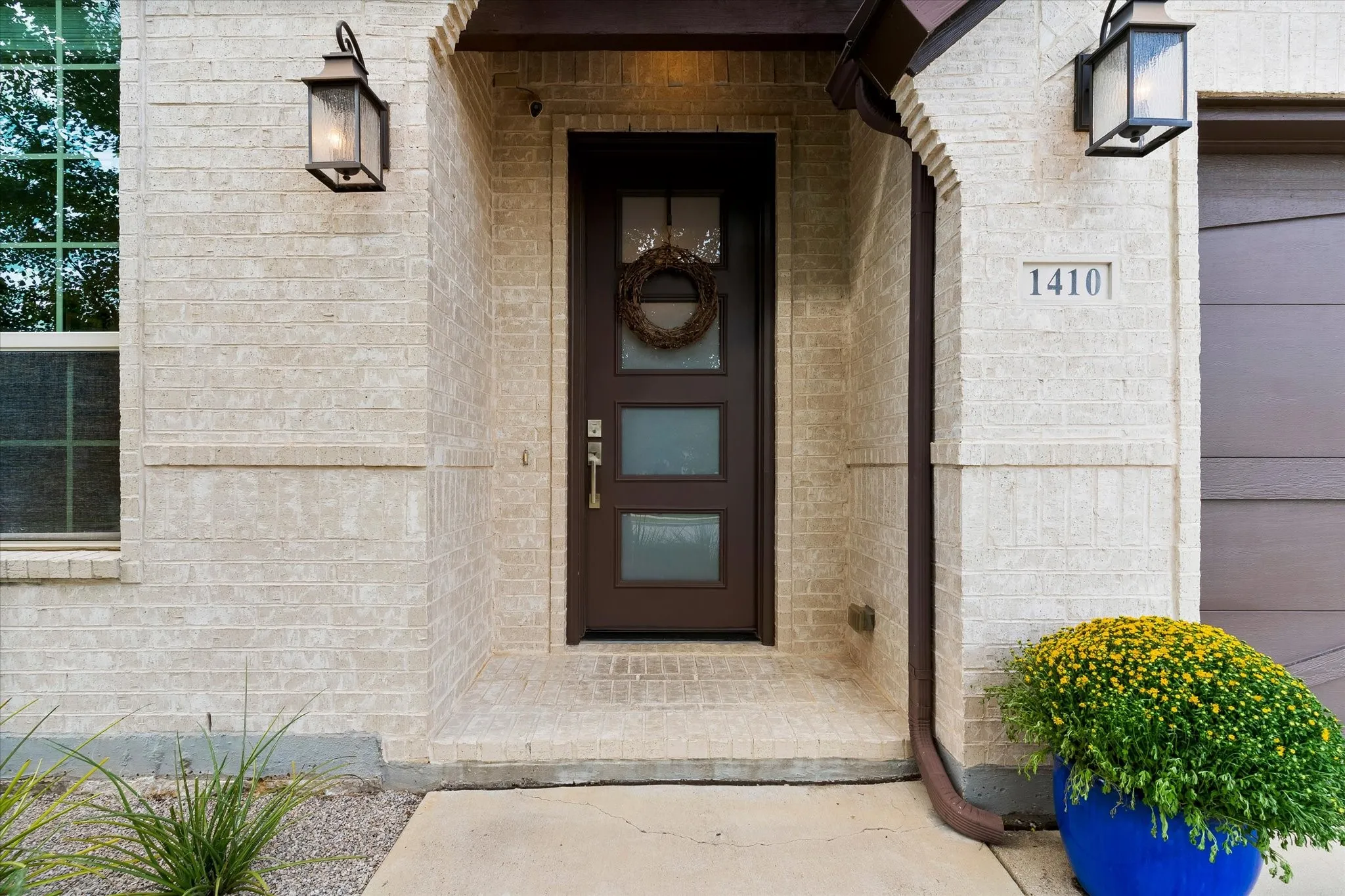 Entryway featuring a modern door with integrated glass panels, brick exterior, two exterior wall sconces, and a rain gutter system