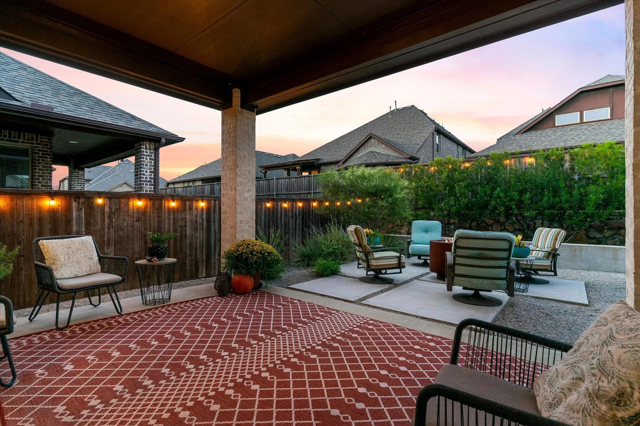 Covered patio with an extended paver and gravel seating area, bordered by mature privacy landscaping and a wood fence