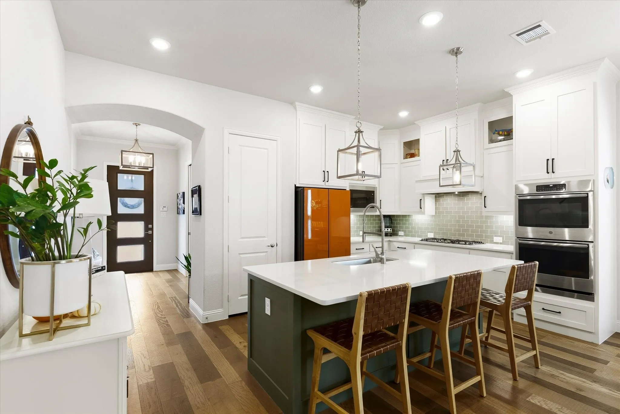 Kitchen island with a white countertop and contrasting base, stainless steel wall ovens, white cabinetry, tile backsplash, and wood-finish flooring