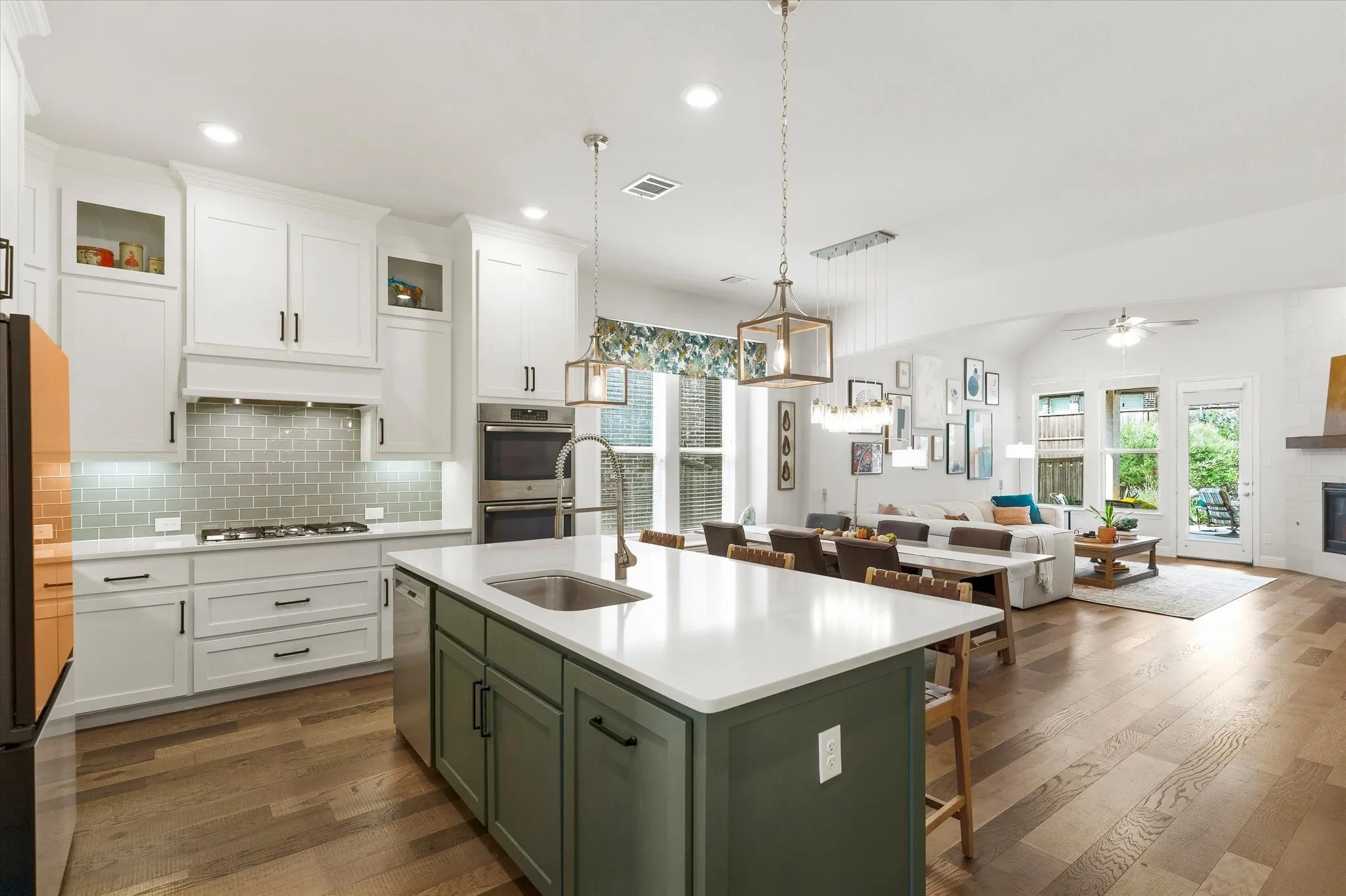 Open-concept living space with wood-finish flooring, white cabinetry, a green kitchen island with a built-in sink, stainless steel appliances, and vaulted ceilings