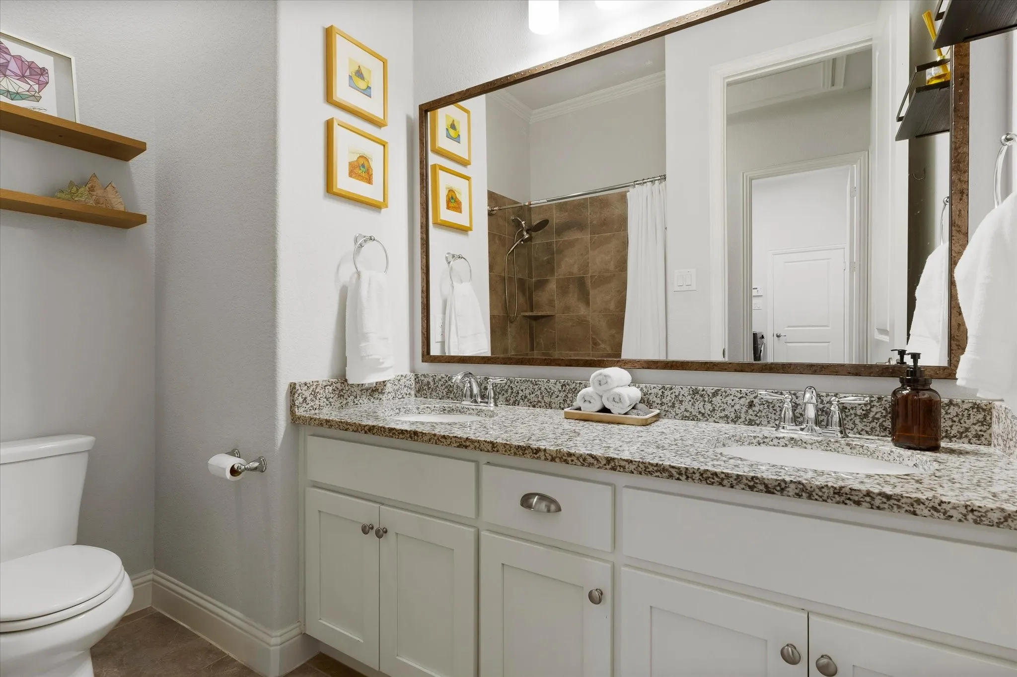 Dual sink vanity with stone countertop, white shaker cabinetry, and large framed mirror