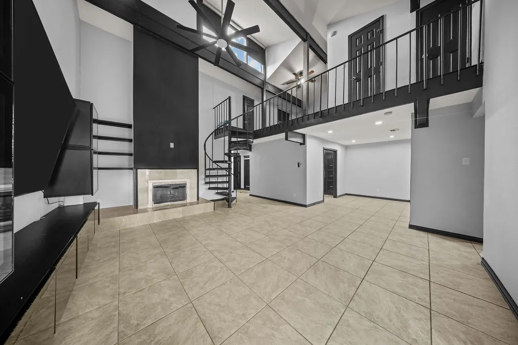 Vaulted ceiling with exposed beams, spiral staircase, fireplace with stone surround, loft with metal railing, and tile flooring
