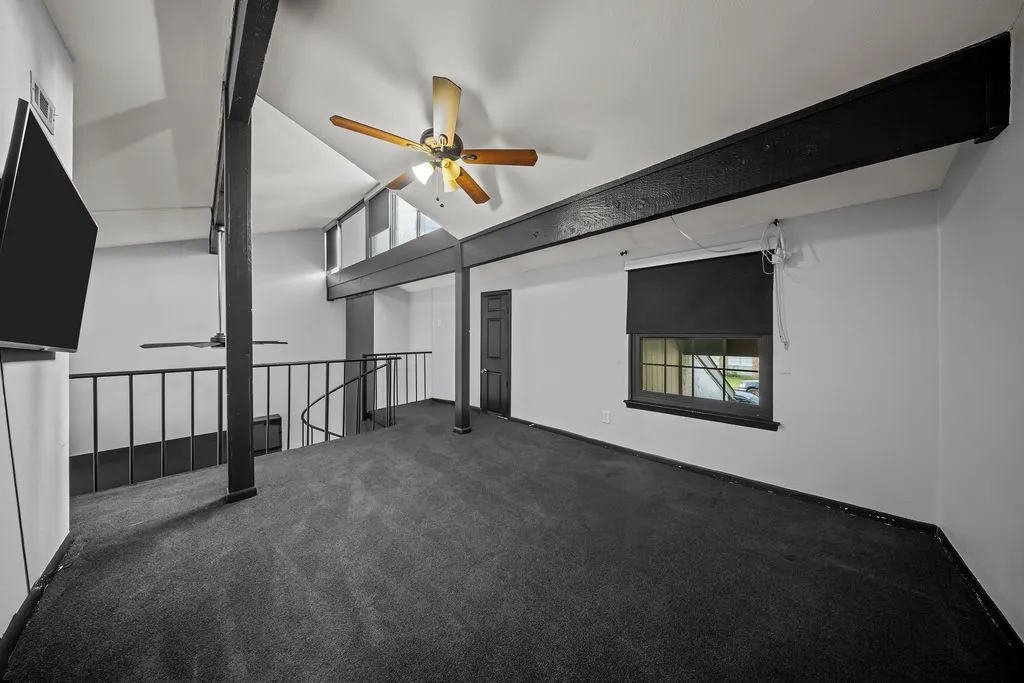 Vaulted ceiling featuring exposed beams, dark carpeting, and a ceiling fan