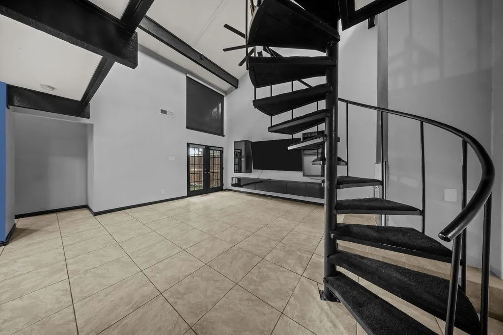 Vaulted ceilings with exposed beams, spiral staircase with carpeted treads, light-toned tile flooring, and double glass-paneled doors