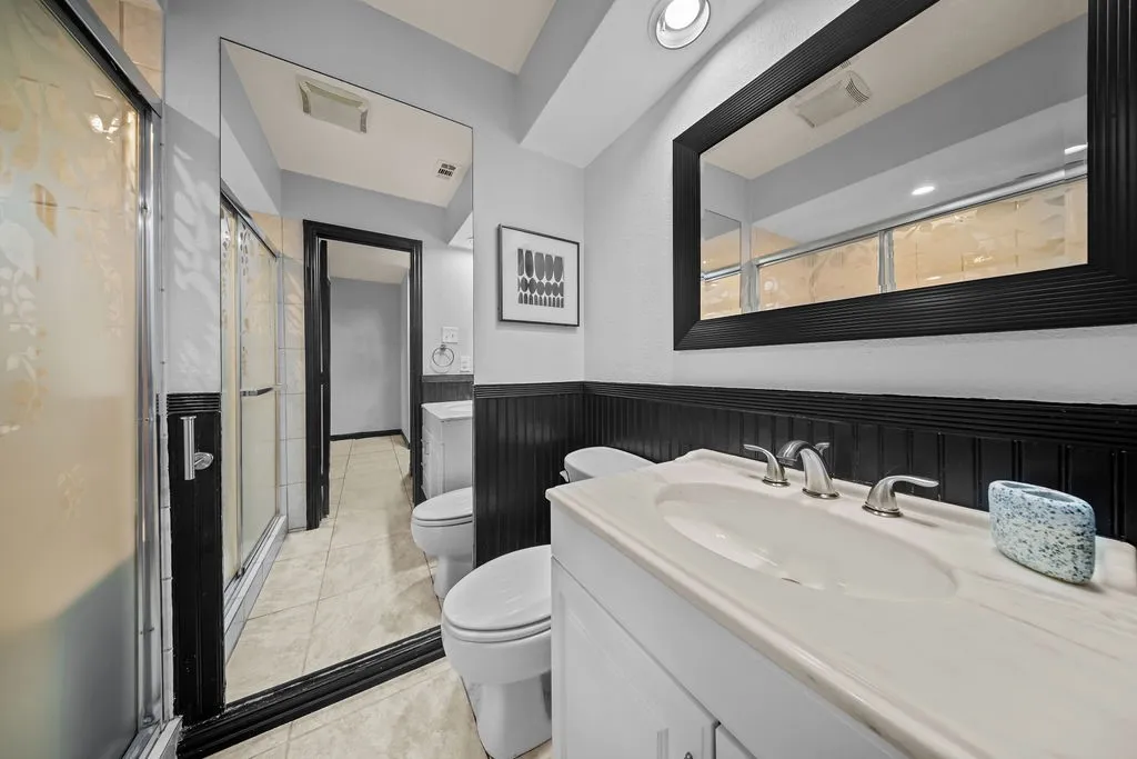 White vanity with an integrated sink and brushed nickel faucet, large framed mirror, vertical wall paneling, and a shower with frosted glass doors