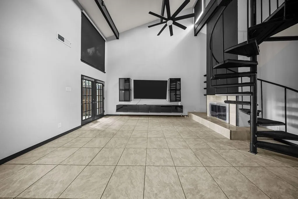 Vaulted ceiling with exposed beams, spiral staircase, floor-to-ceiling fireplace, tile flooring, and glass-paneled double doors