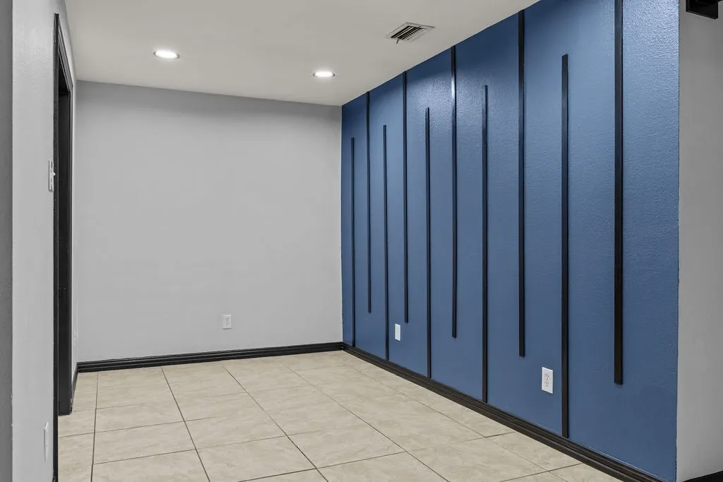 Recessed ceiling lighting, blue accent wall with vertical paneling, light-colored tile flooring, and dark trim