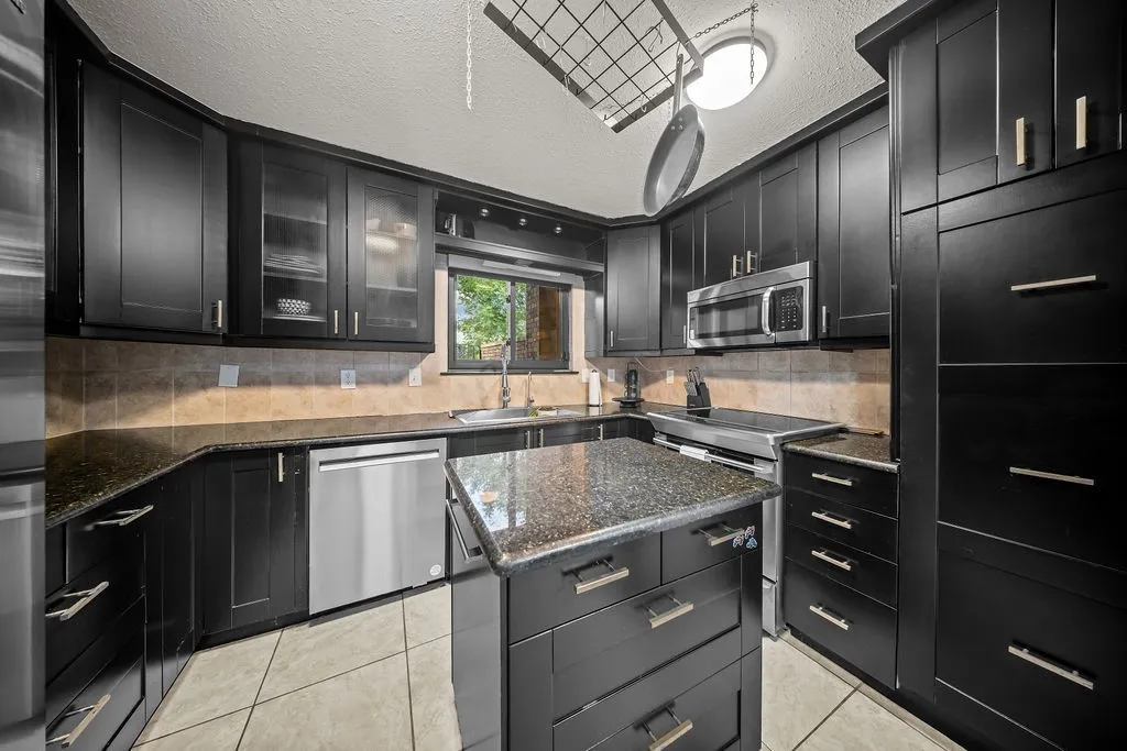 Black cabinetry with brushed nickel hardware, granite countertops, stainless steel appliances, and a tiled backsplash