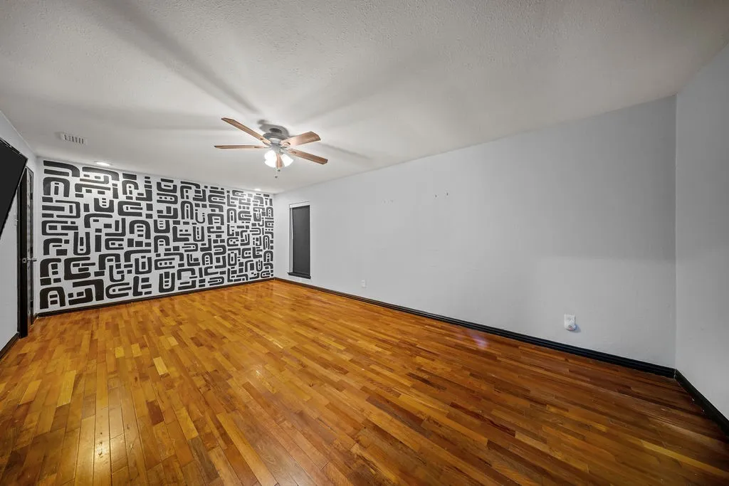 Wood-finish flooring, ceiling fan with light fixture, and a decorative accent wall