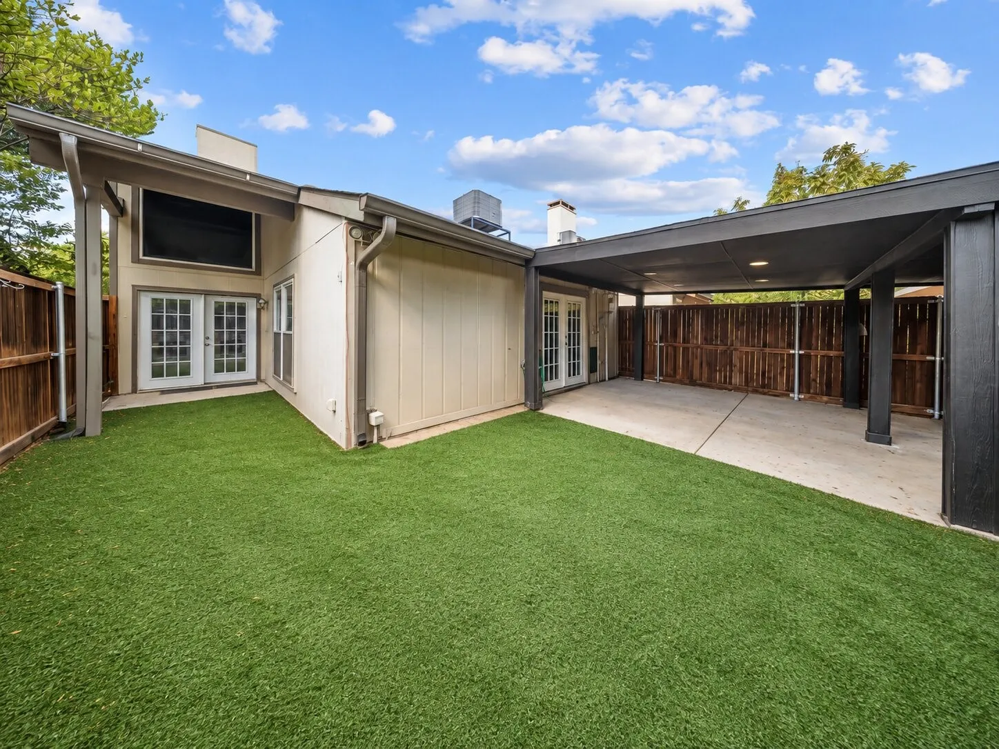 Expansive artificial turf backyard with a covered patio, French doors, and a detached carport