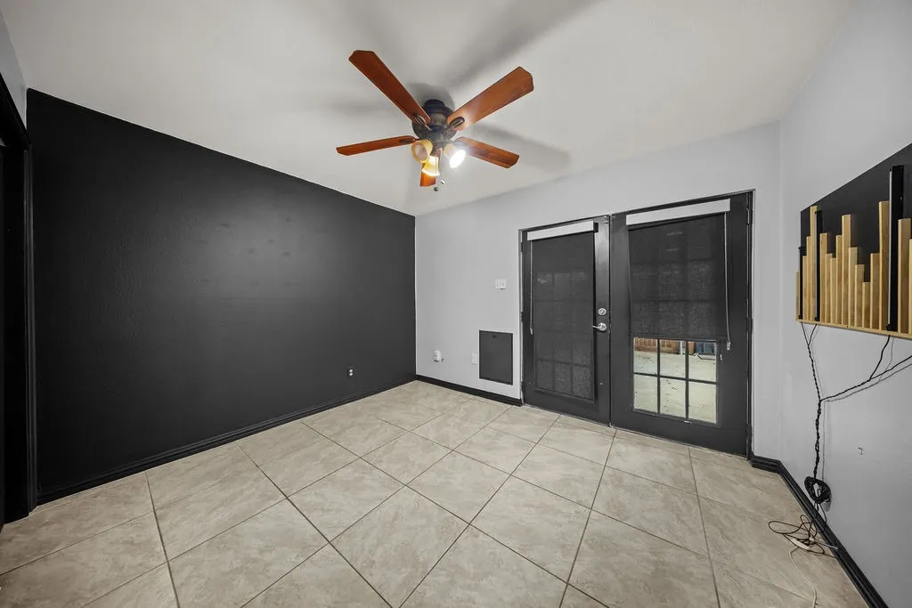 Ceramic tile flooring, black accent wall, ceiling fan with light fixture, and French doors with privacy screens